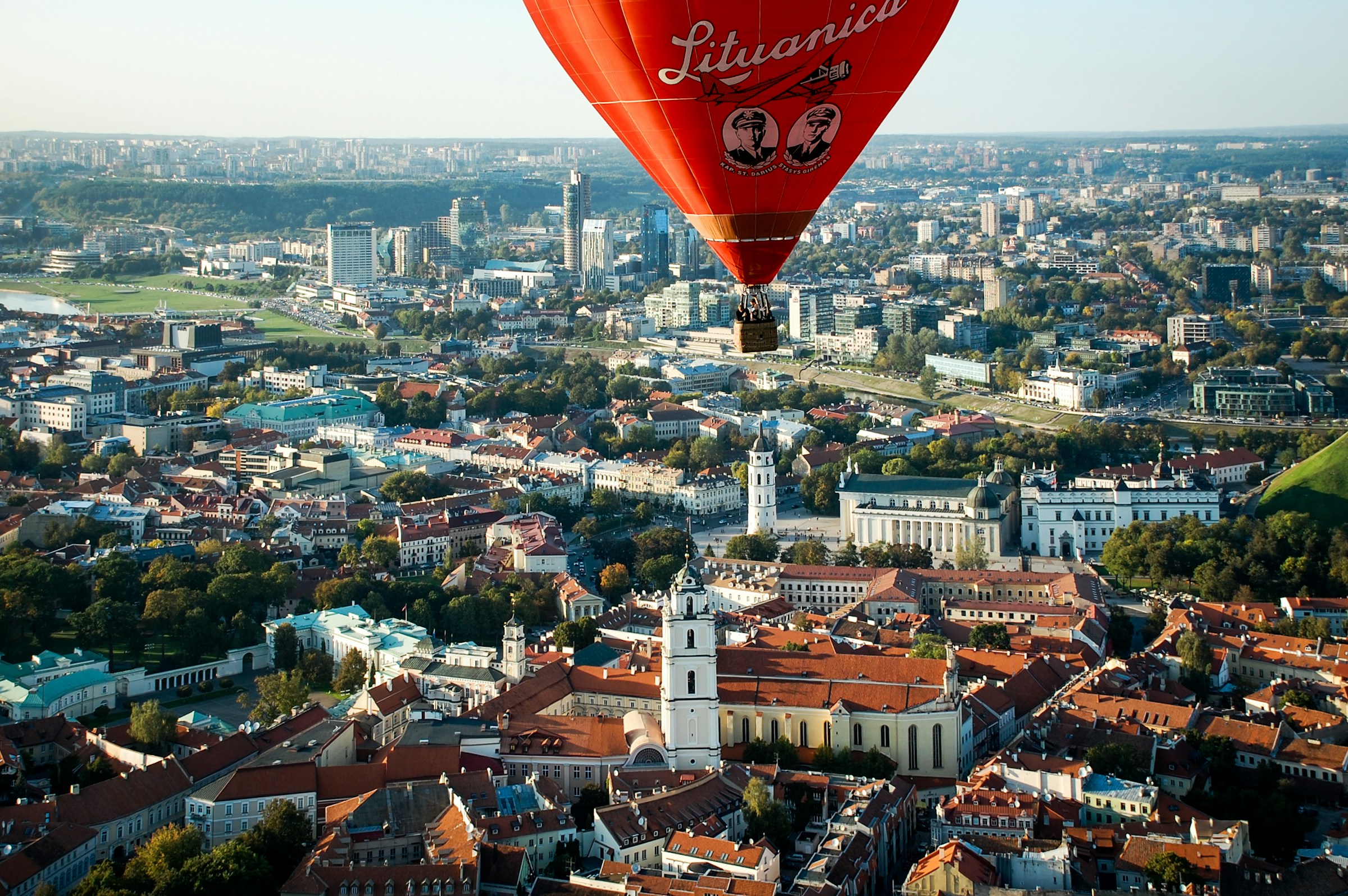 Red hot air balloon over Vilnius, Lithuania cityscape, featuring historic buildings and greenery under a clear sky