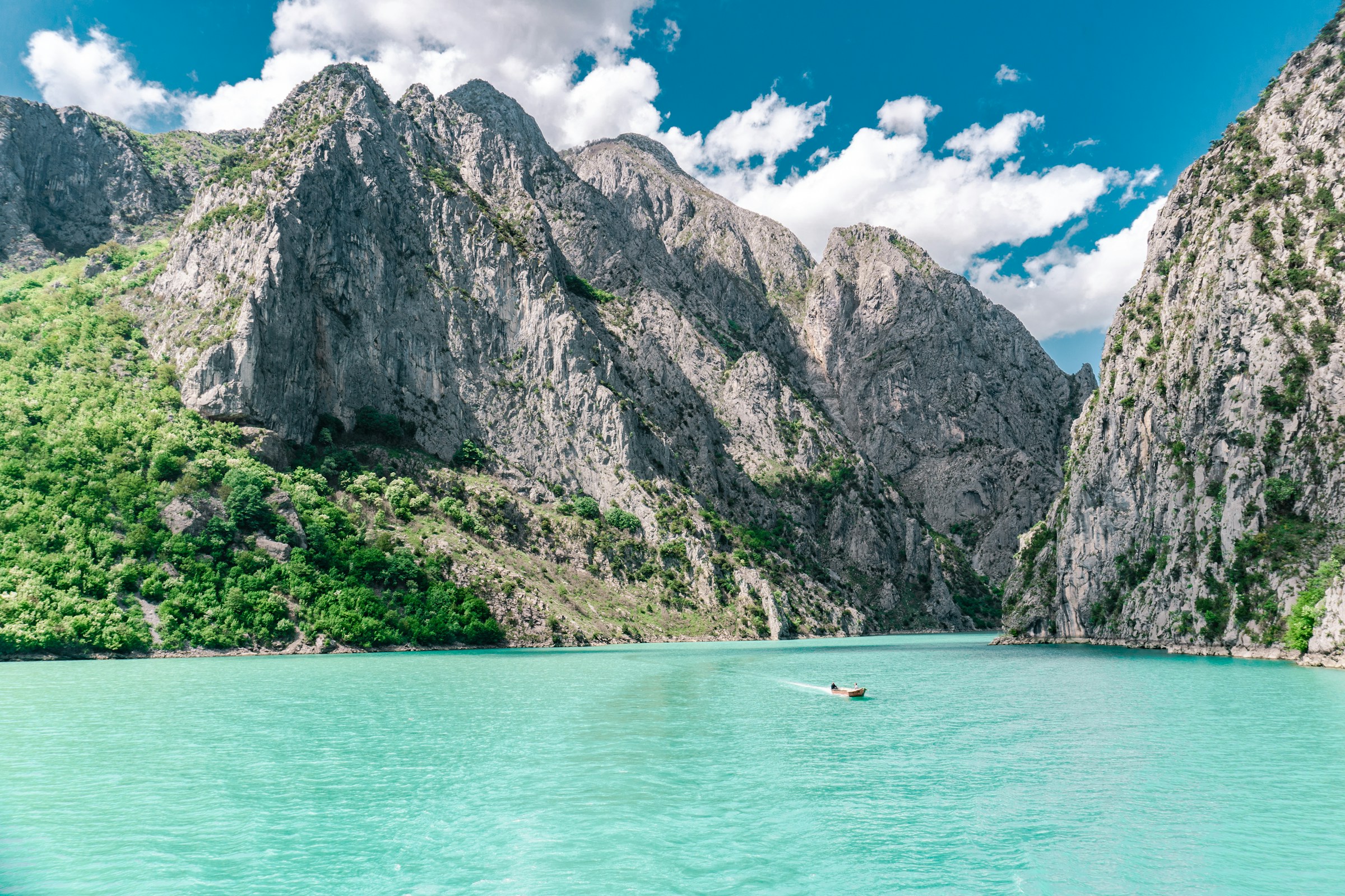 Turquoise waters and a small boat surrounded by lush green mountains and rocky cliffs in Albania. 