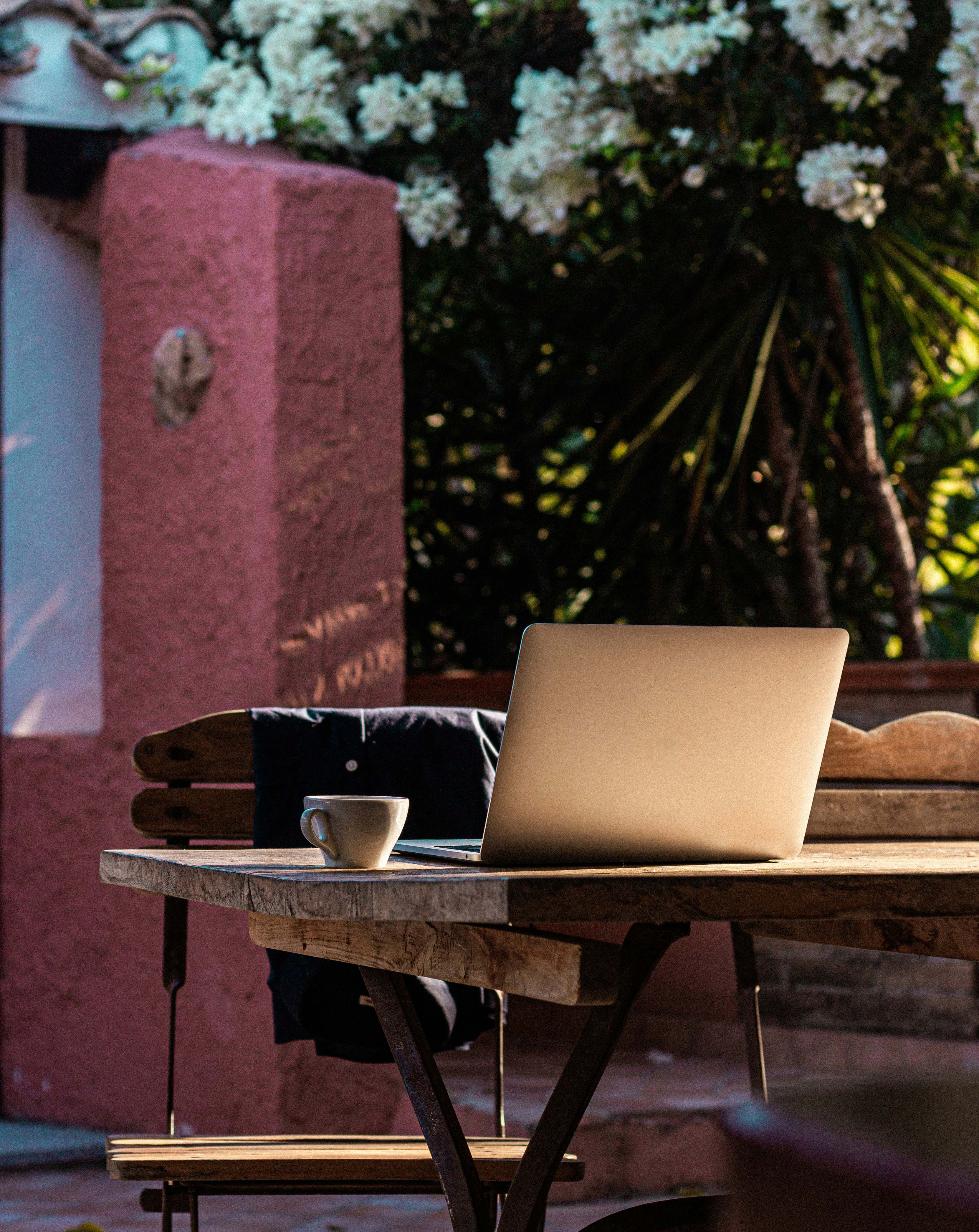 Laptop and coffee at a café or hotel in a quiet outdoor environment. Image illustrating bleisure, remote work, and the flexibility to combine work with vacation.