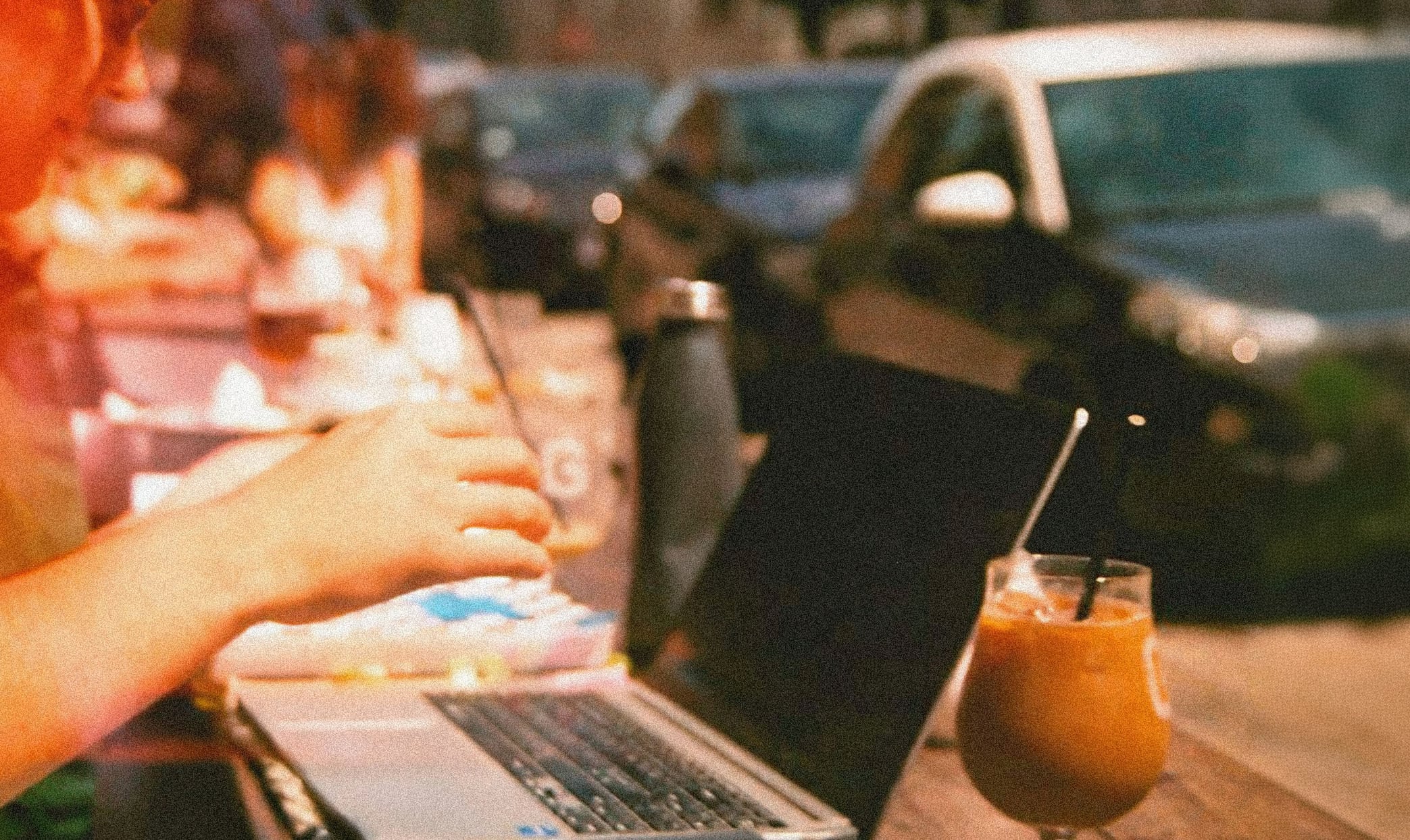 Person som jobber på en laptop fra en kafé under en campingtur. Bilde som illustrerer hvordan forretningsreiser kan kombineres med ferie, fjernarbeid og fleksibilitet.