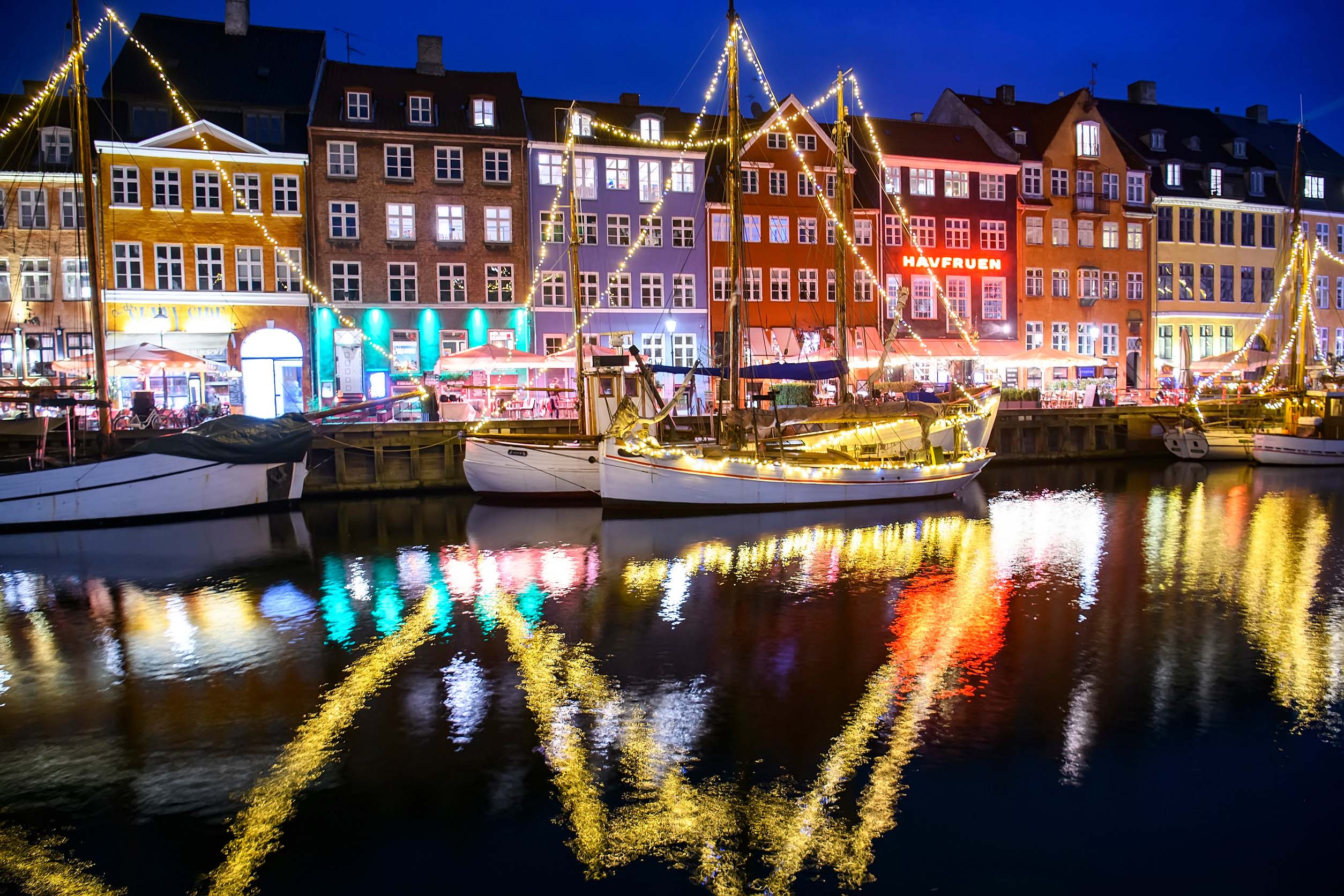 Boats decorated with Christmas lights reflected in the water at Nyhavn harbour in Copenhagen during winter