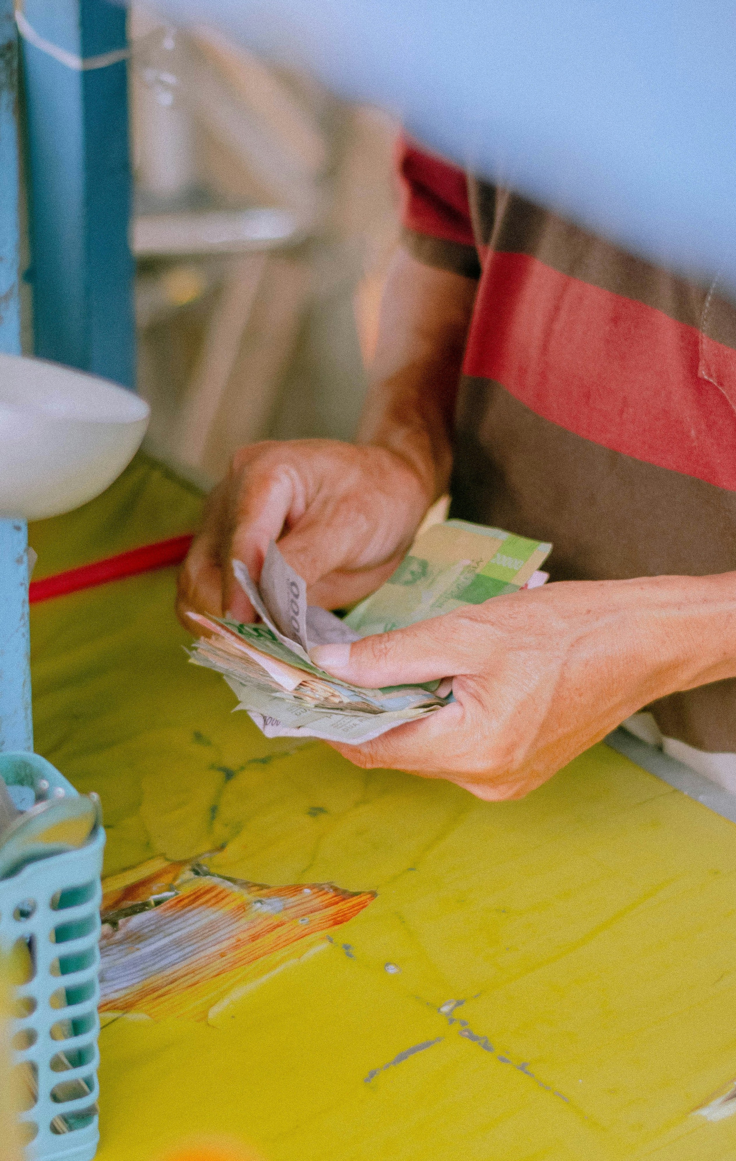 Person teller papirpenger på et gult bord i en uformell setting.