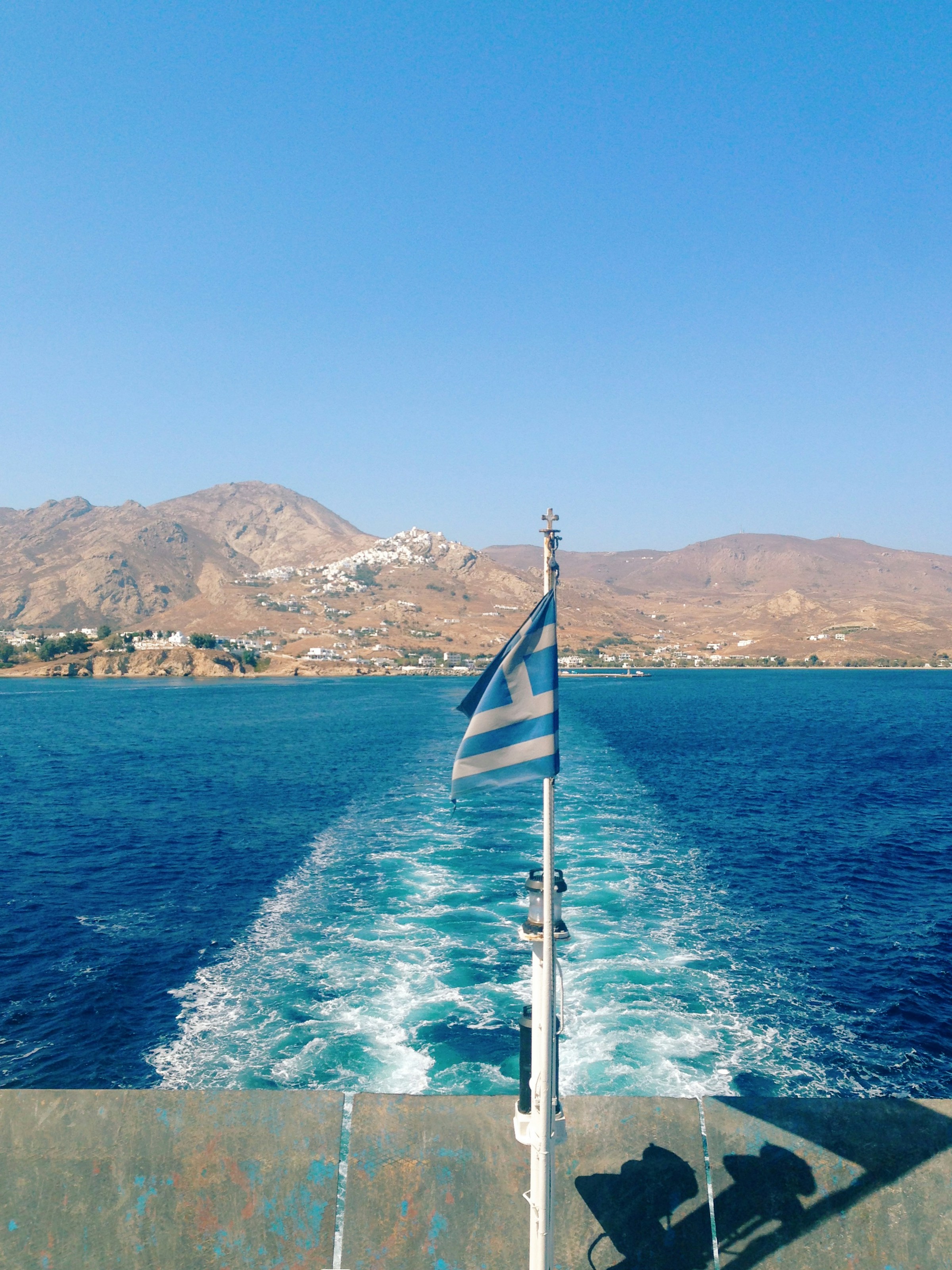 Greek flag in the stern of a boat with the sea behind it and an island in the background