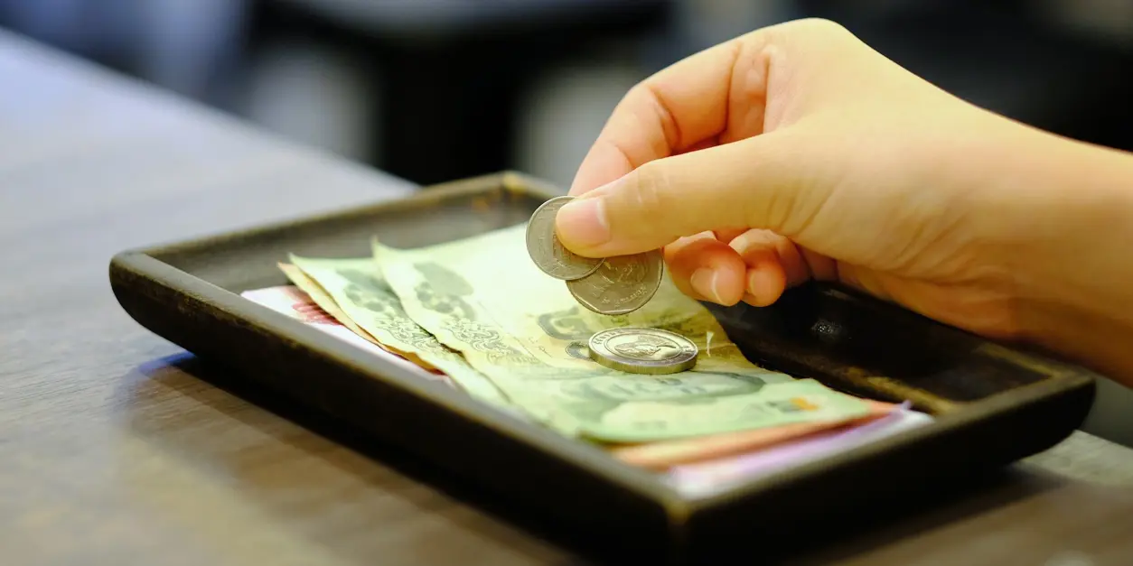 Hand l&auml;gger mynt p&aring; en bricka med sedlar och mynt, troligen som betalning eller dricks p&aring; en restaurang.