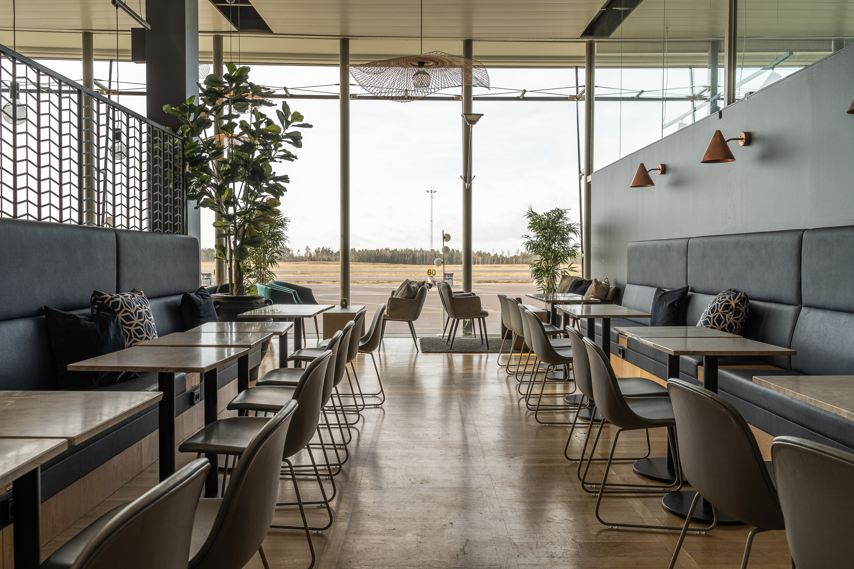A restaurant environment with rows of tables and chairs, upholstered benches along the walls and large windows overlooking an open landscape.