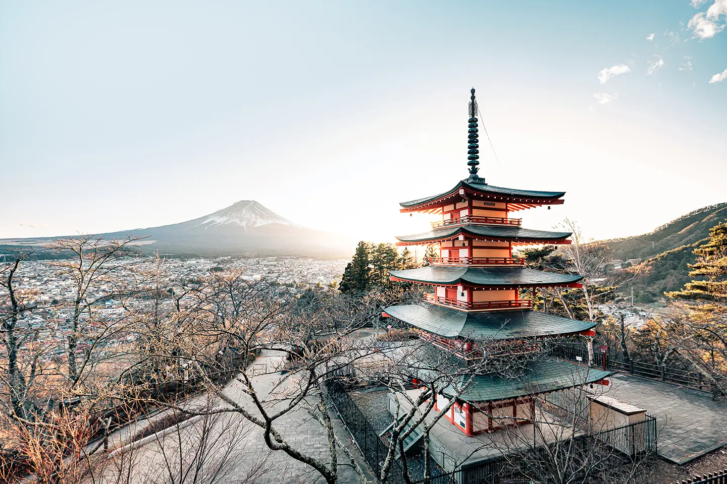 Chureito Pagoda with Mount Fuji in the background during sunset, surrounded by trees and overlooking the cityscape in Japan.
