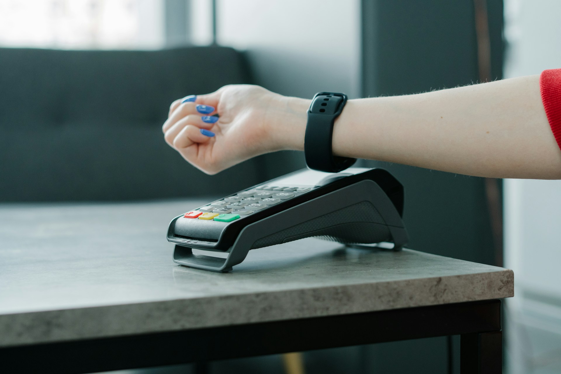 A person makes a contactless payment with a smartwatch at a payment terminal on a table.