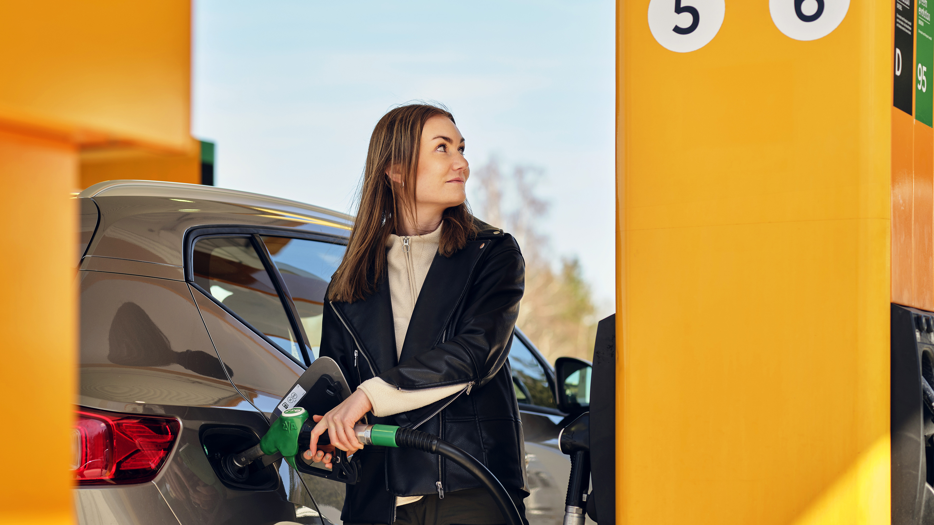 Woman with sunglasses on head smiling in bright setting, wearing a striped shirt, near a window with sunlit background.
