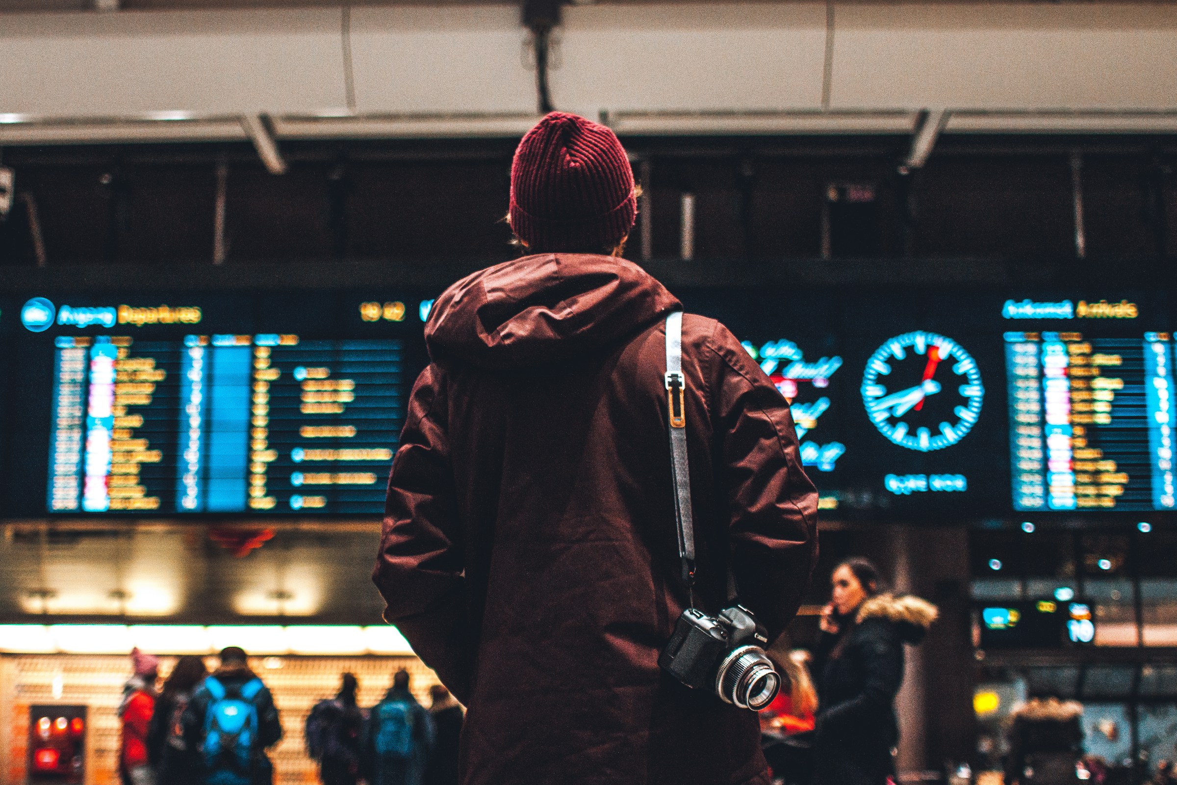 Traveler with camera at airport, viewing flight departure board.