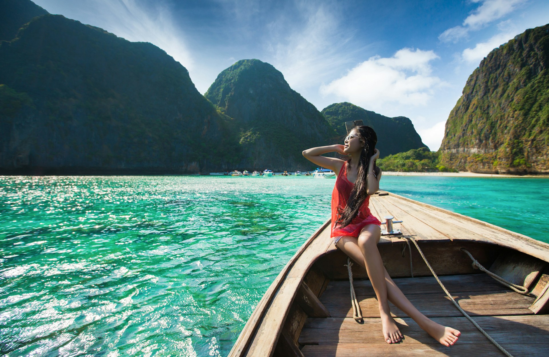 Woman sitting at the front of a longtail boat in Thailand going over clear blue sea with mountains in the background