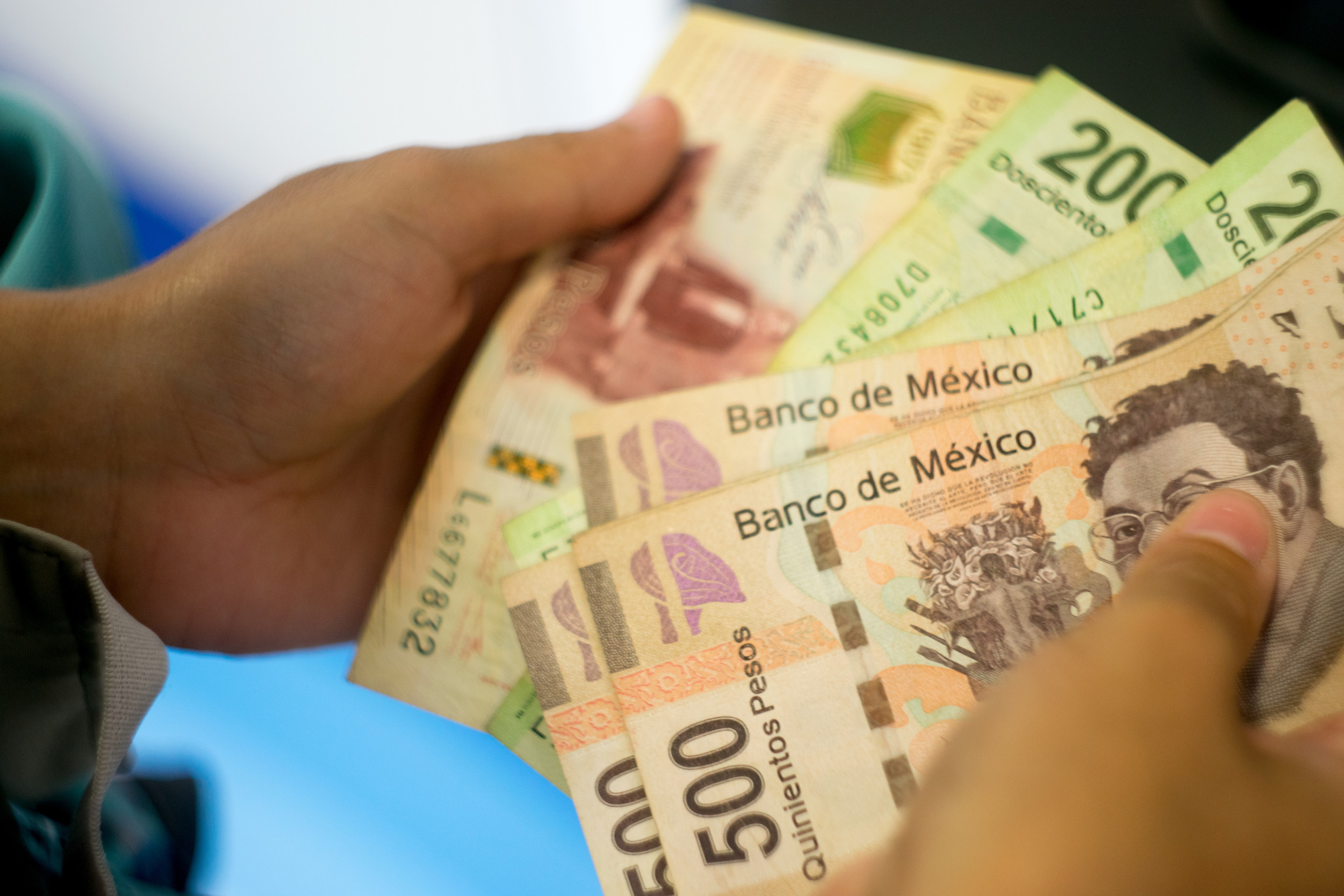Person har meksikanske pesos i forskjellige valører, inkludert 500 og 200 sedler, med teksten "Banco de México".