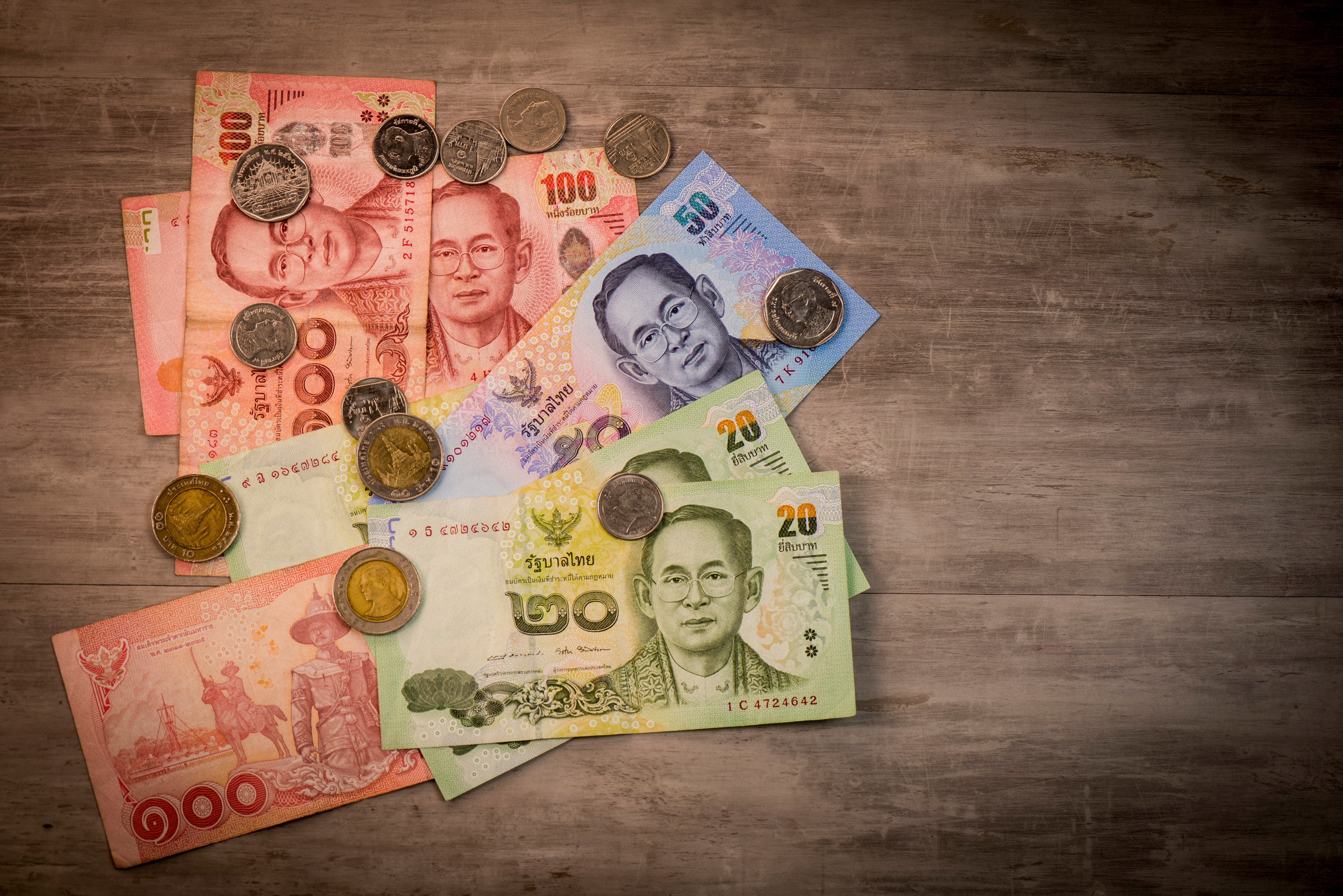 Thailandske baht-sedler og mynter spredt på tregulv.