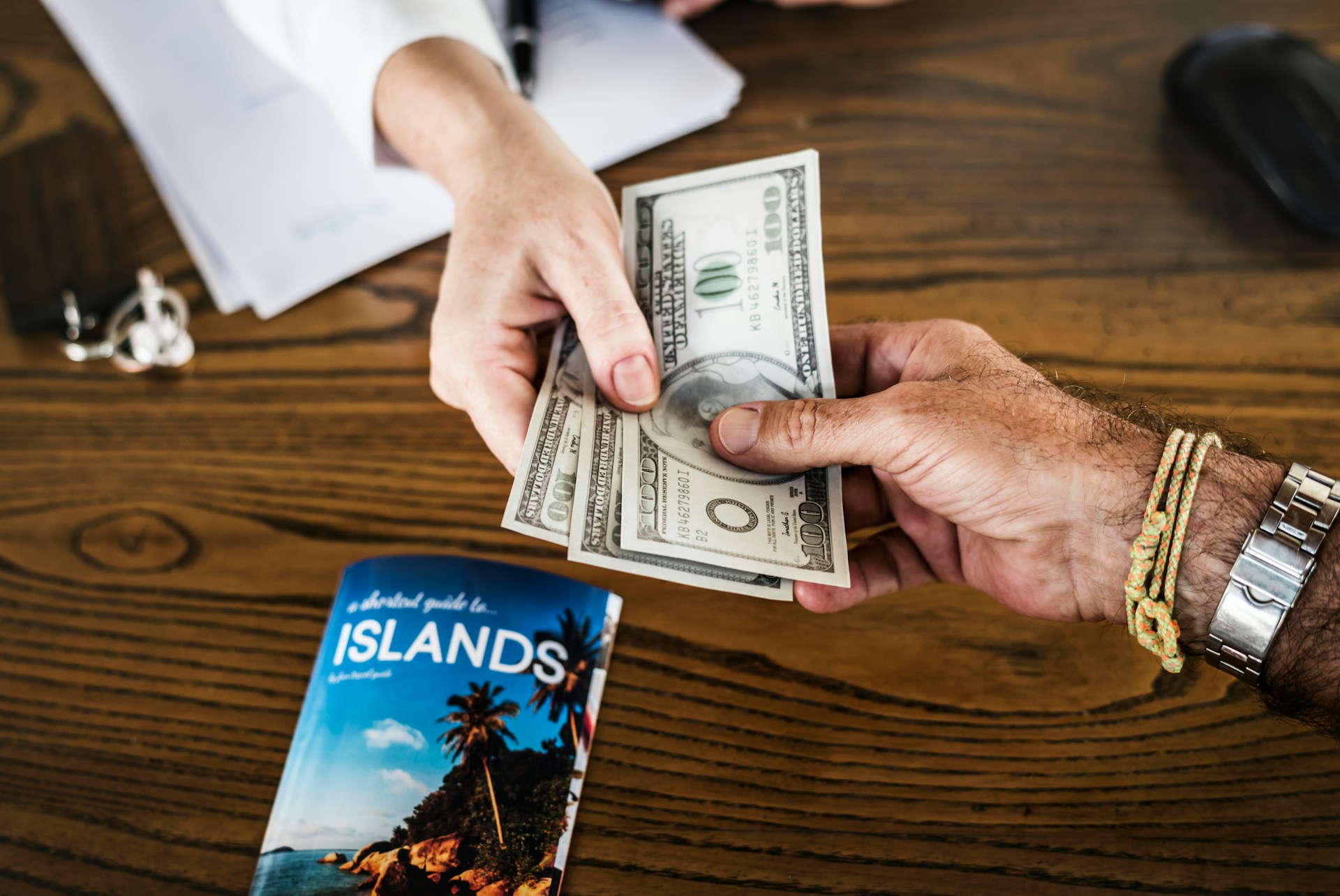 Person exchanging cash for a travel catalog of islands on a table.