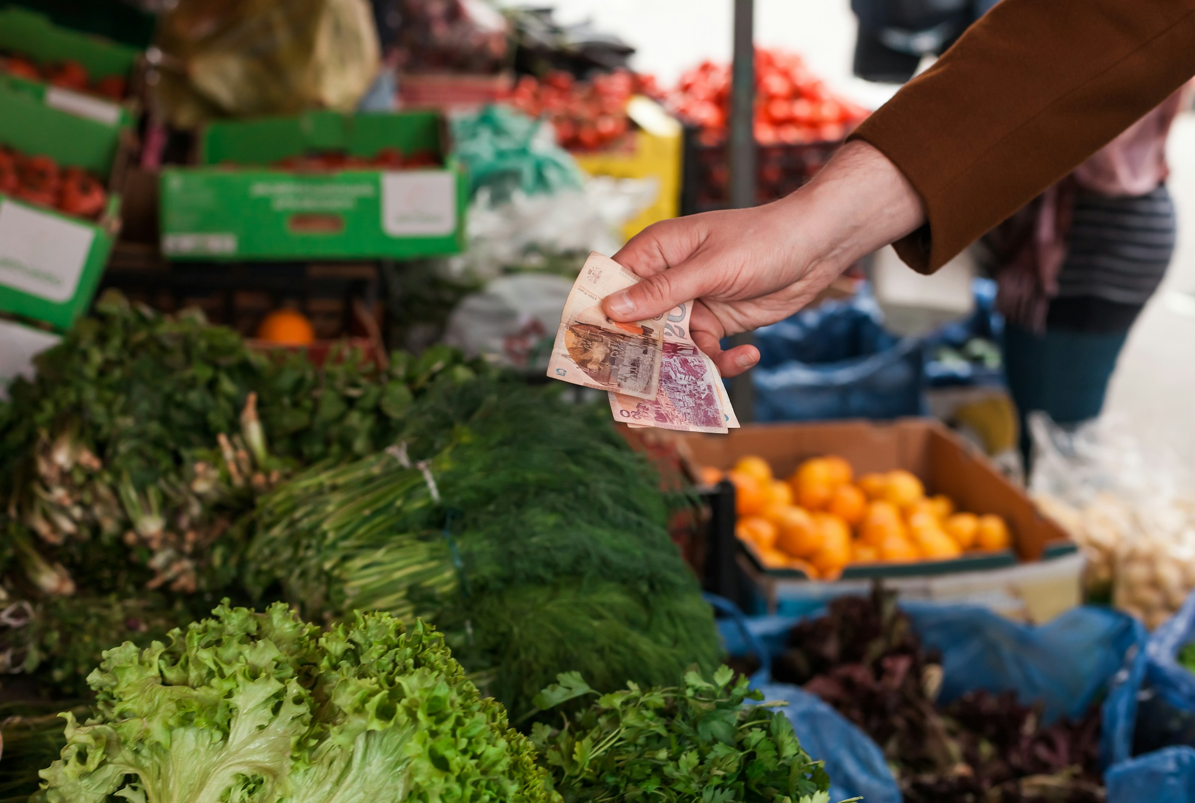 Person kjøper grønnsaker på et utendørsmarked og beholder penger over ferske salathoder og andre grønnsaker i Sverige.