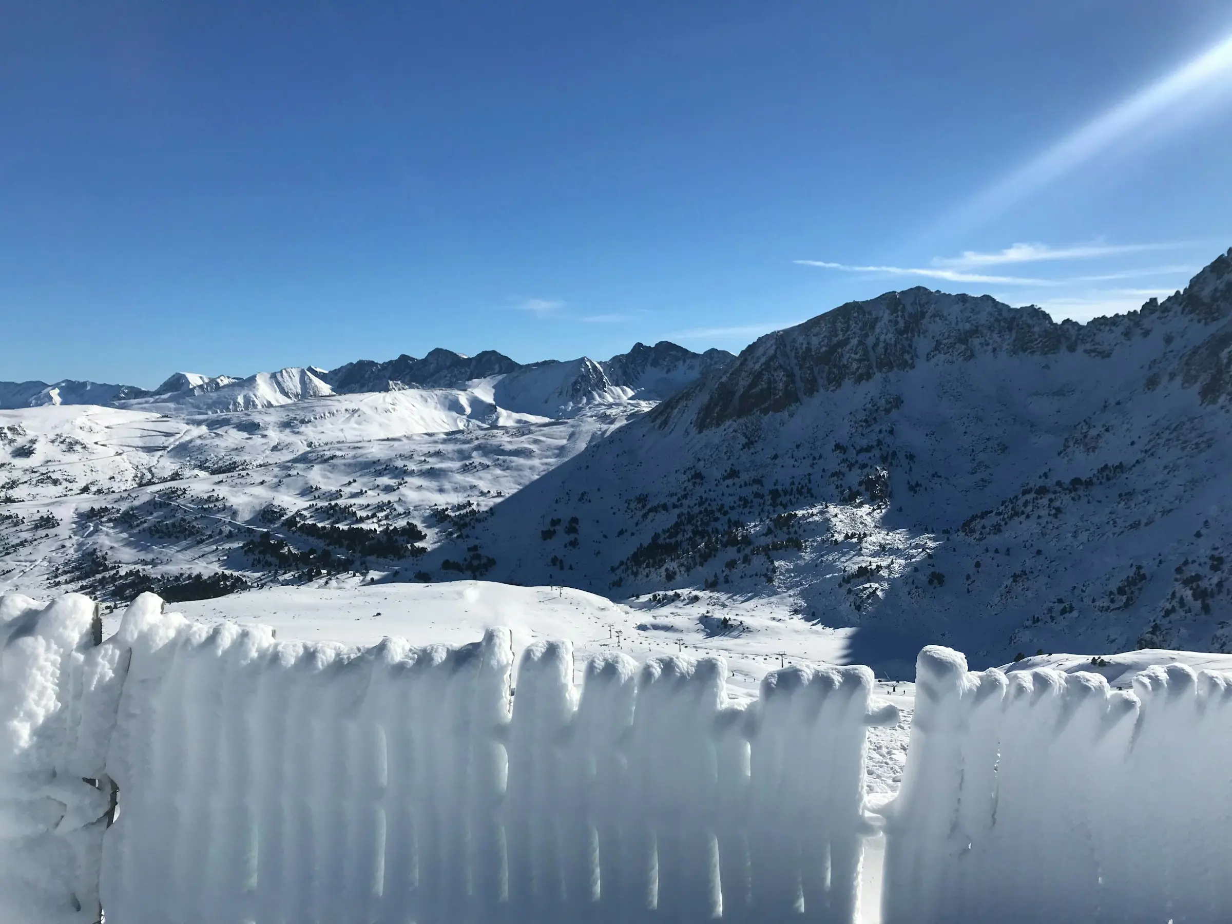 Snødekt vinterlandskap som fører opp til mektige fjell og blå himmel i Grandvalira, Andorra