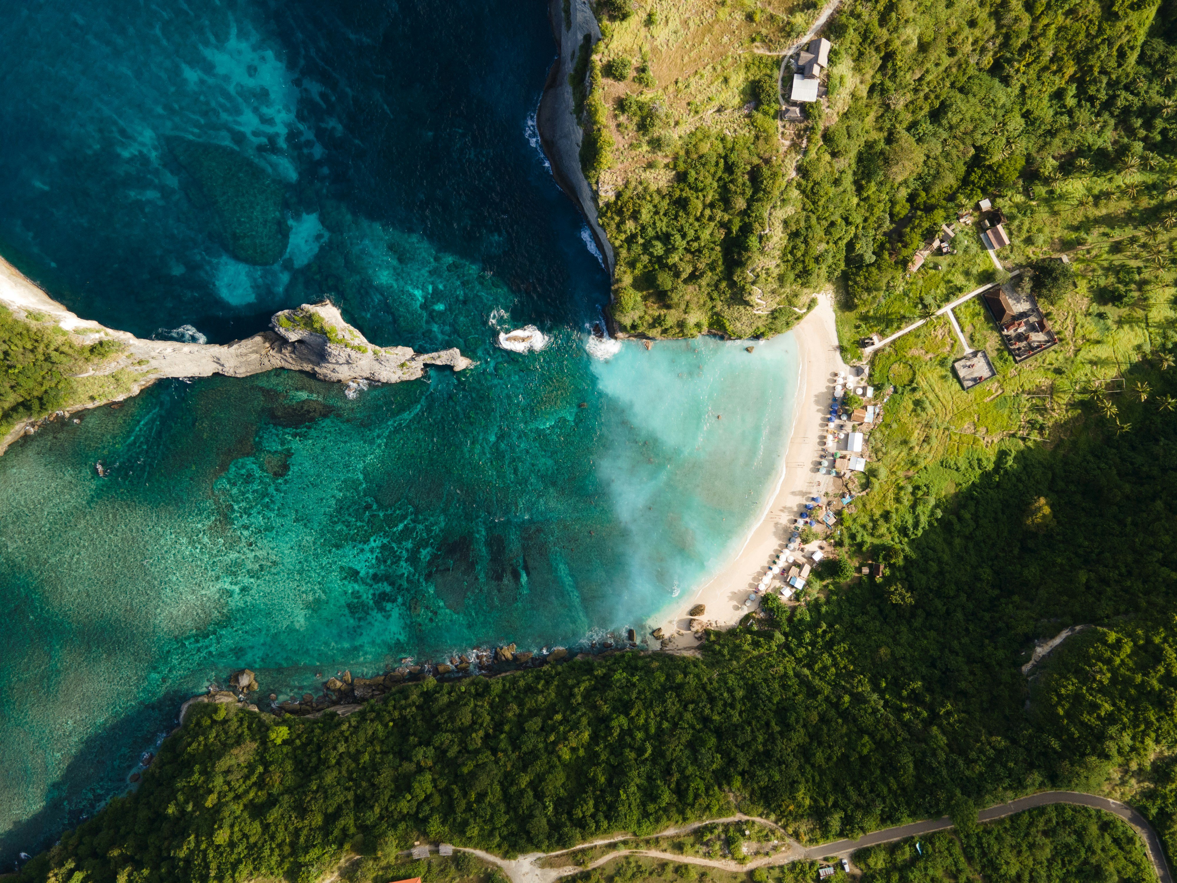 Travel to Bali - Aerial view of a tropical beach with turquoise waters, white sand, and lush green cliffs on Nusa Penida Island, Indonesia.