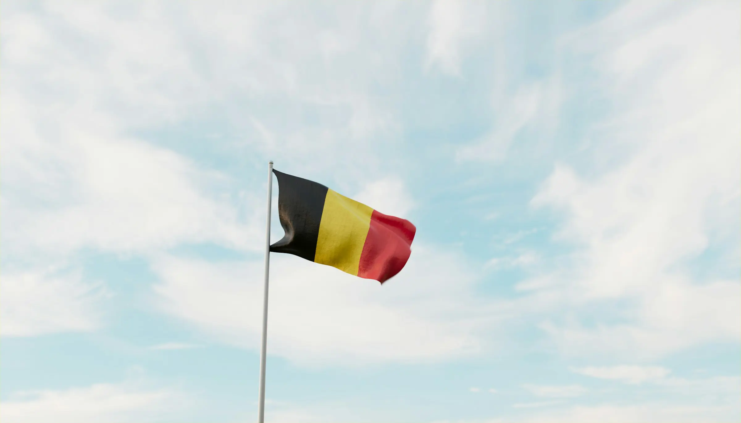 Belgium flag waving against a blue sky with clouds.