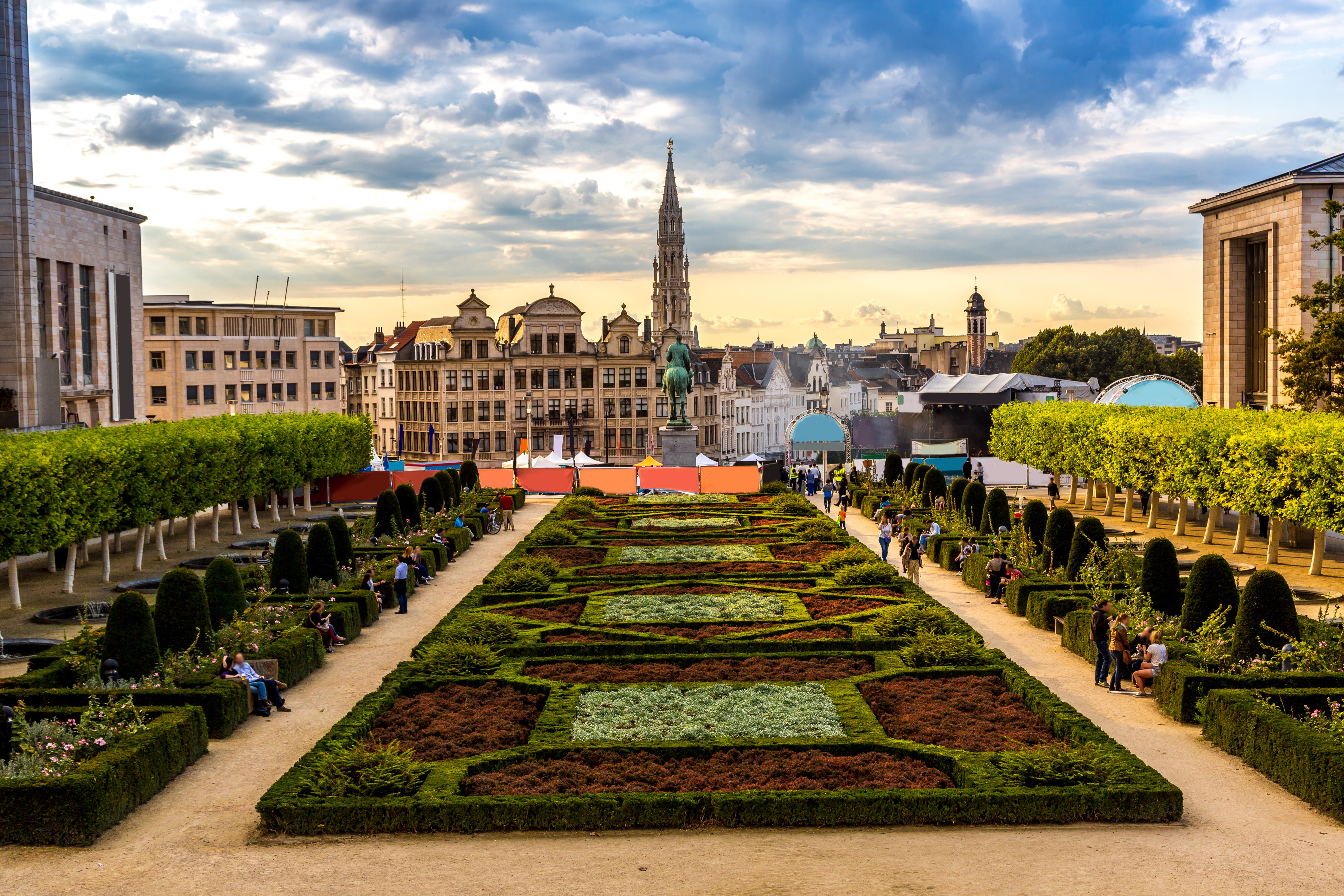 Travel to Brussels - View of Mont des Arts gardens featuring manicured hedges, colorful flowerbeds, and a backdrop of historic buildings under a partly cloudy sky.