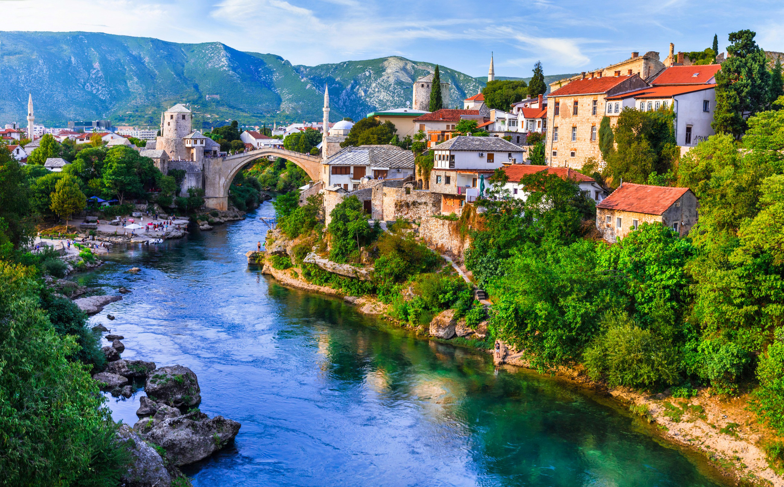 Utsikt over den historiske byen Mostar med Stari Most-broen over elven Neretva, omgitt av frodig natur og gamle bygninger