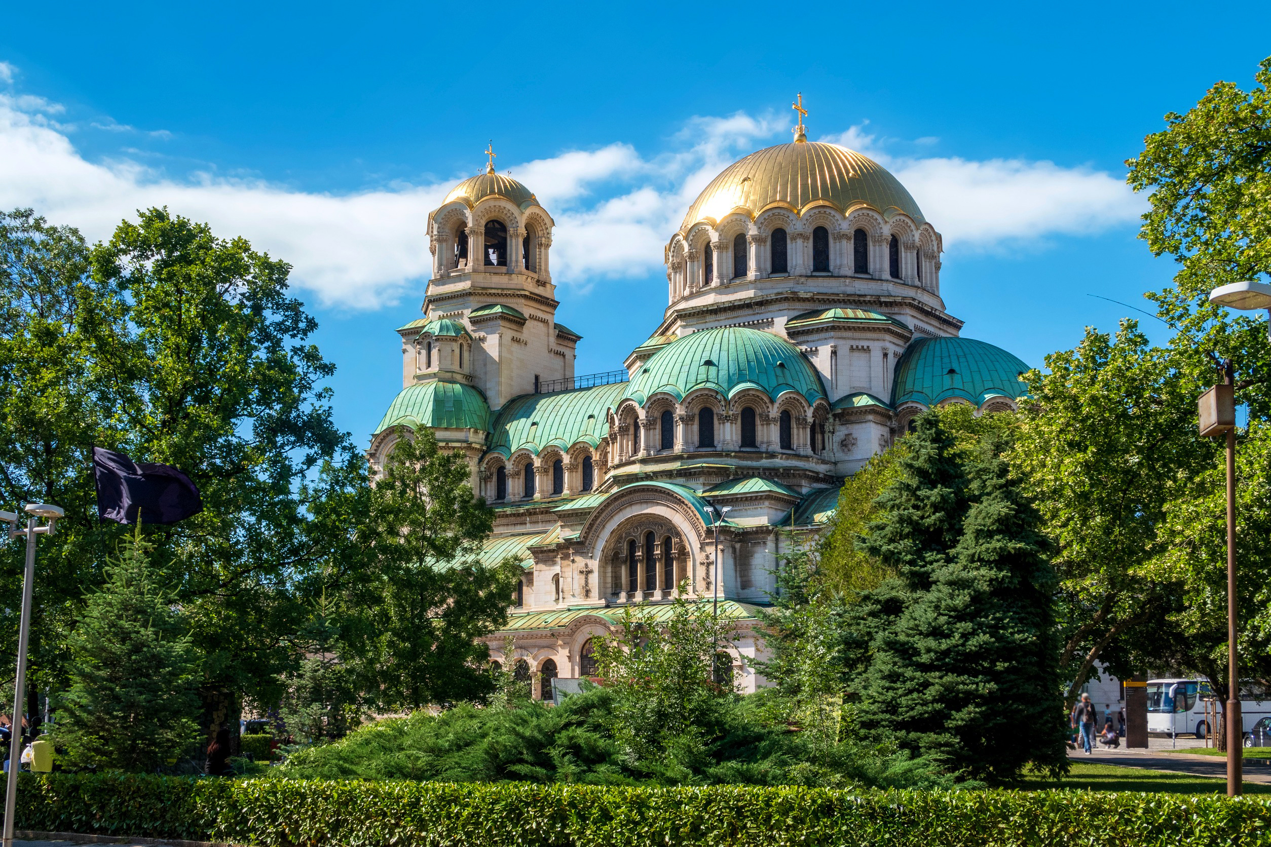 St. Aleksander Nevskij-katedralen i Sofia, Bulgaria, med sine karakteristiske gyldne og grønne kupler, omgitt av frodige trær og en klar blå himmel
