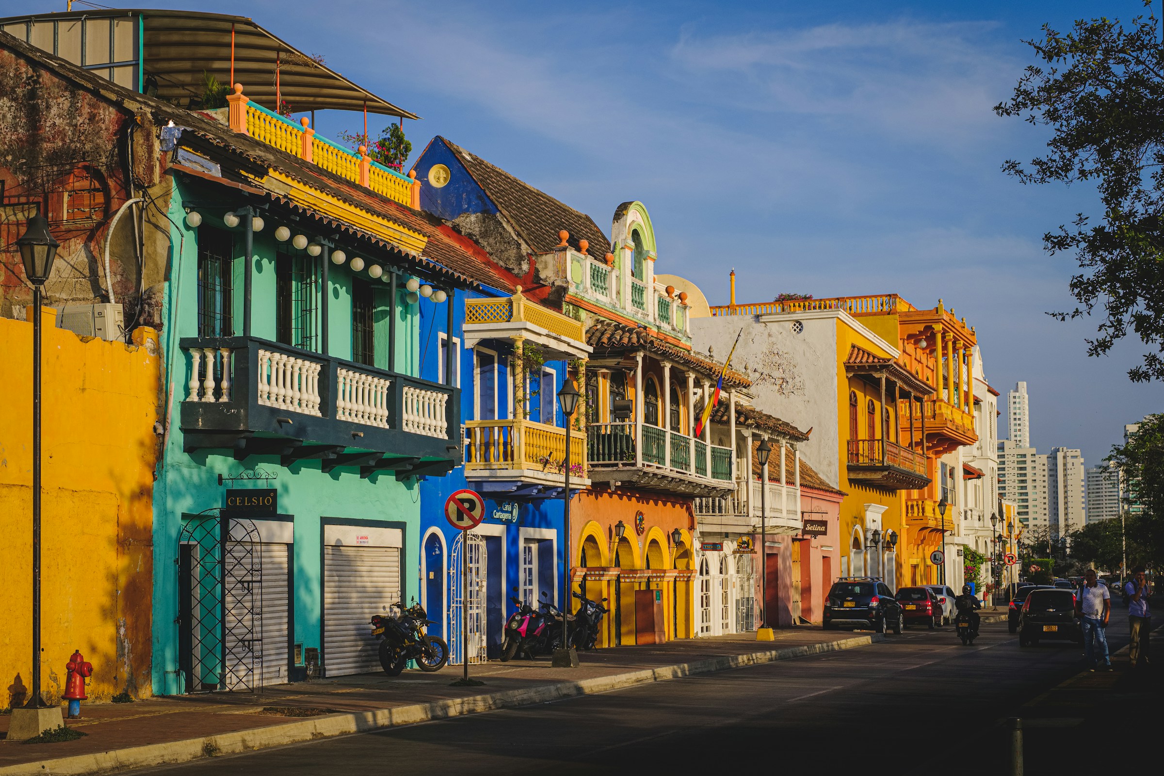 Colorful colonial buildings lining a street in Cartagena, Colombia, with vibrant facades and balconies under a clear blue sky.