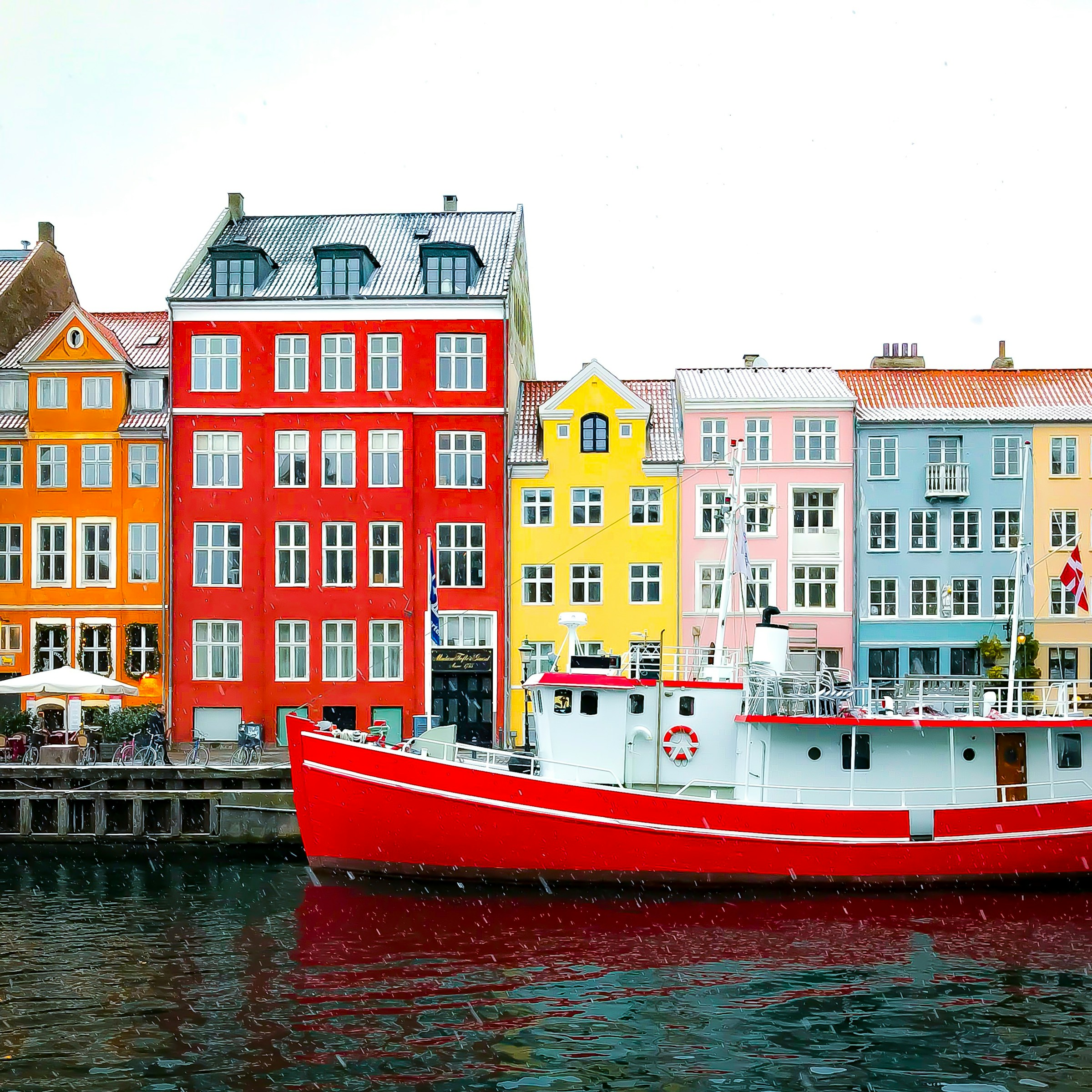 Colorful buildings line the waterfront in Nyhavn, Copenhagen, with a red boat in the foreground reflecting in the canal.