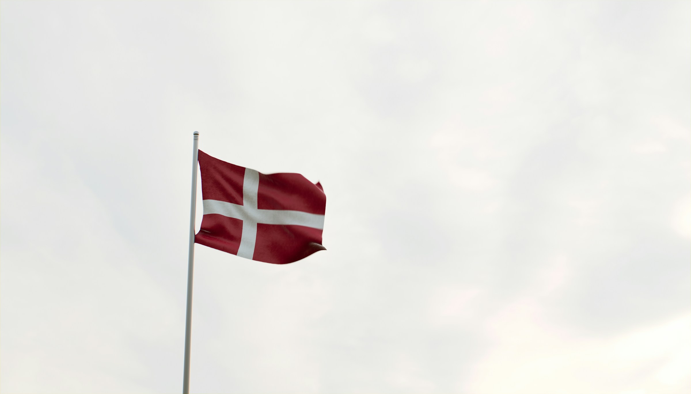 Danish flag, known as the Dannebrog, waving against a cloudy sky.