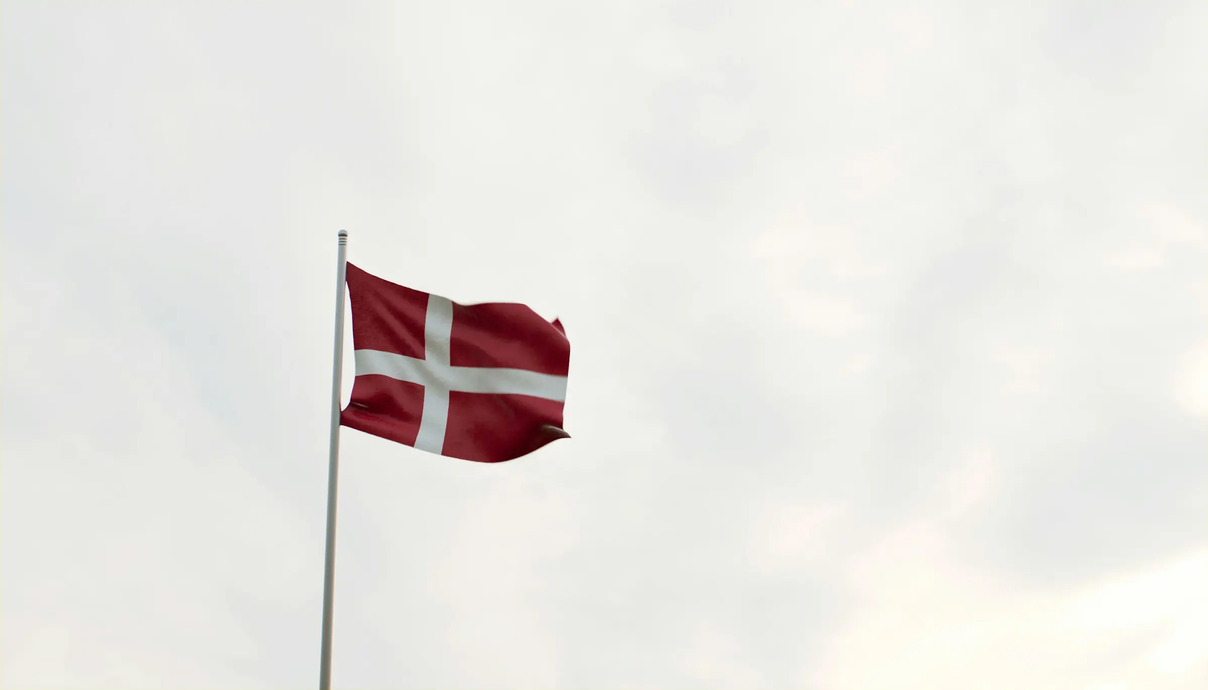 Danish flag, known as the Dannebrog, waving against a cloudy sky.