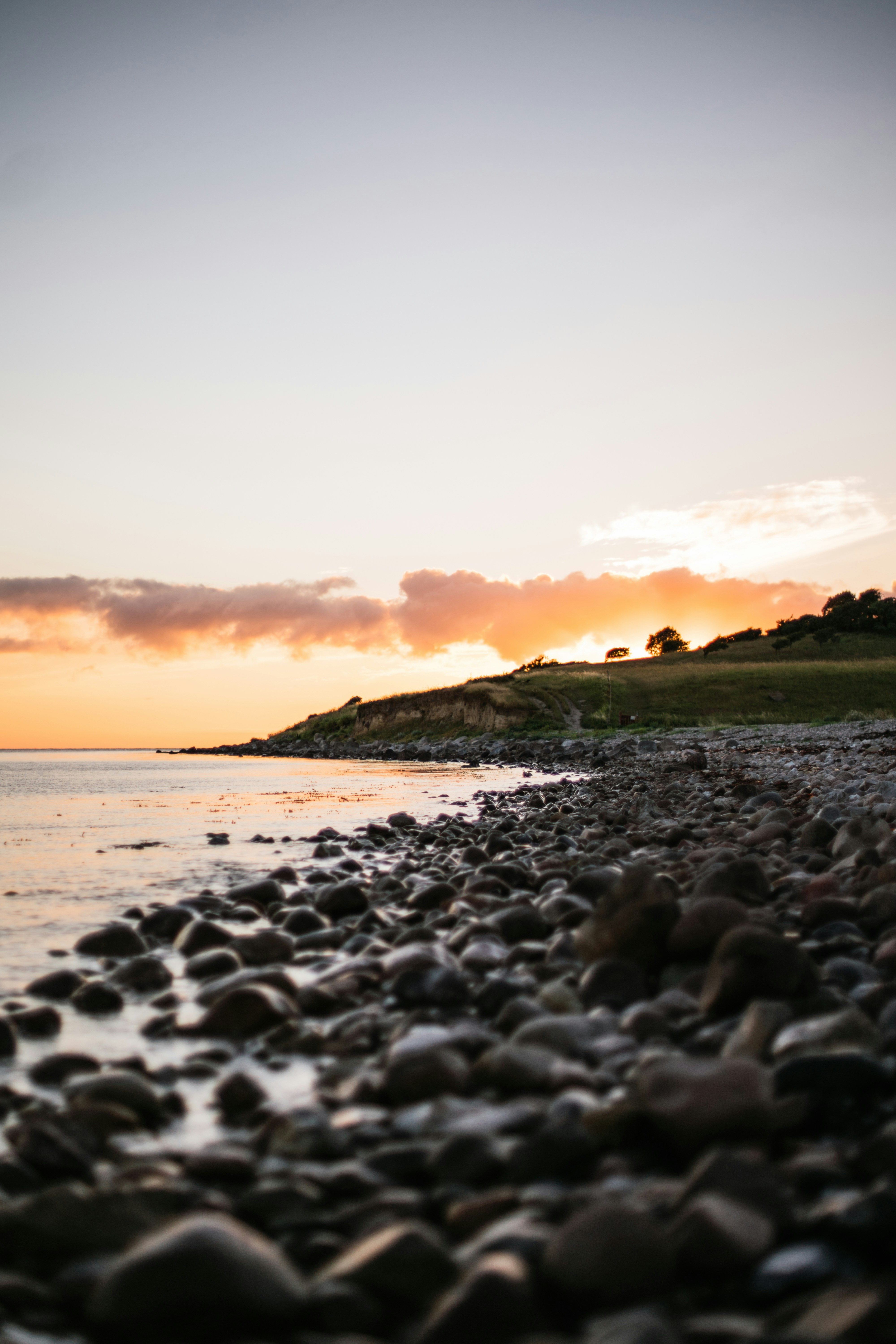 Steinstrand ved solnedgang med oransje og rosa skyer over horisonten