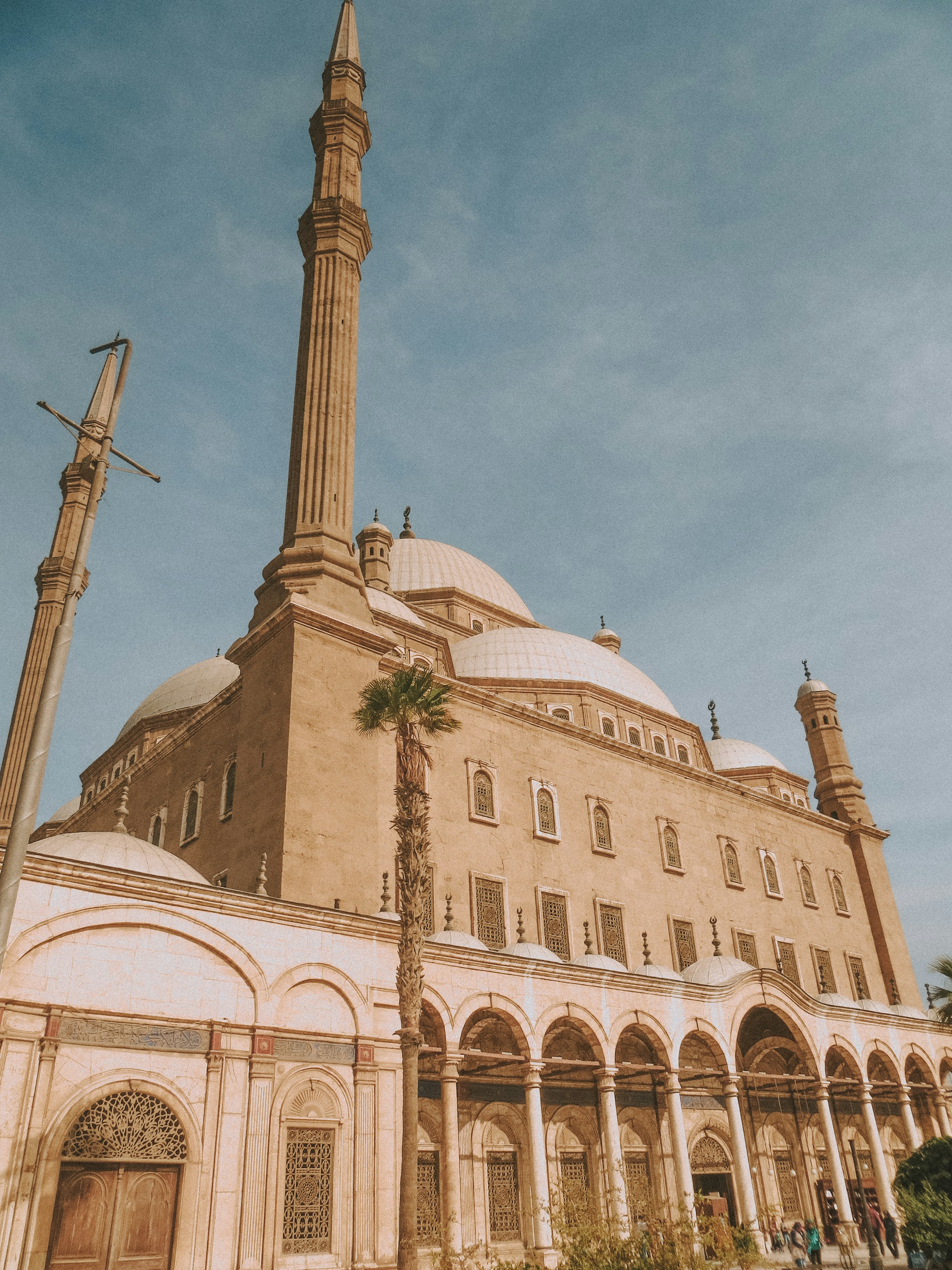 Historic mosque exterior with large domes and towering minarets against a clear blue sky.