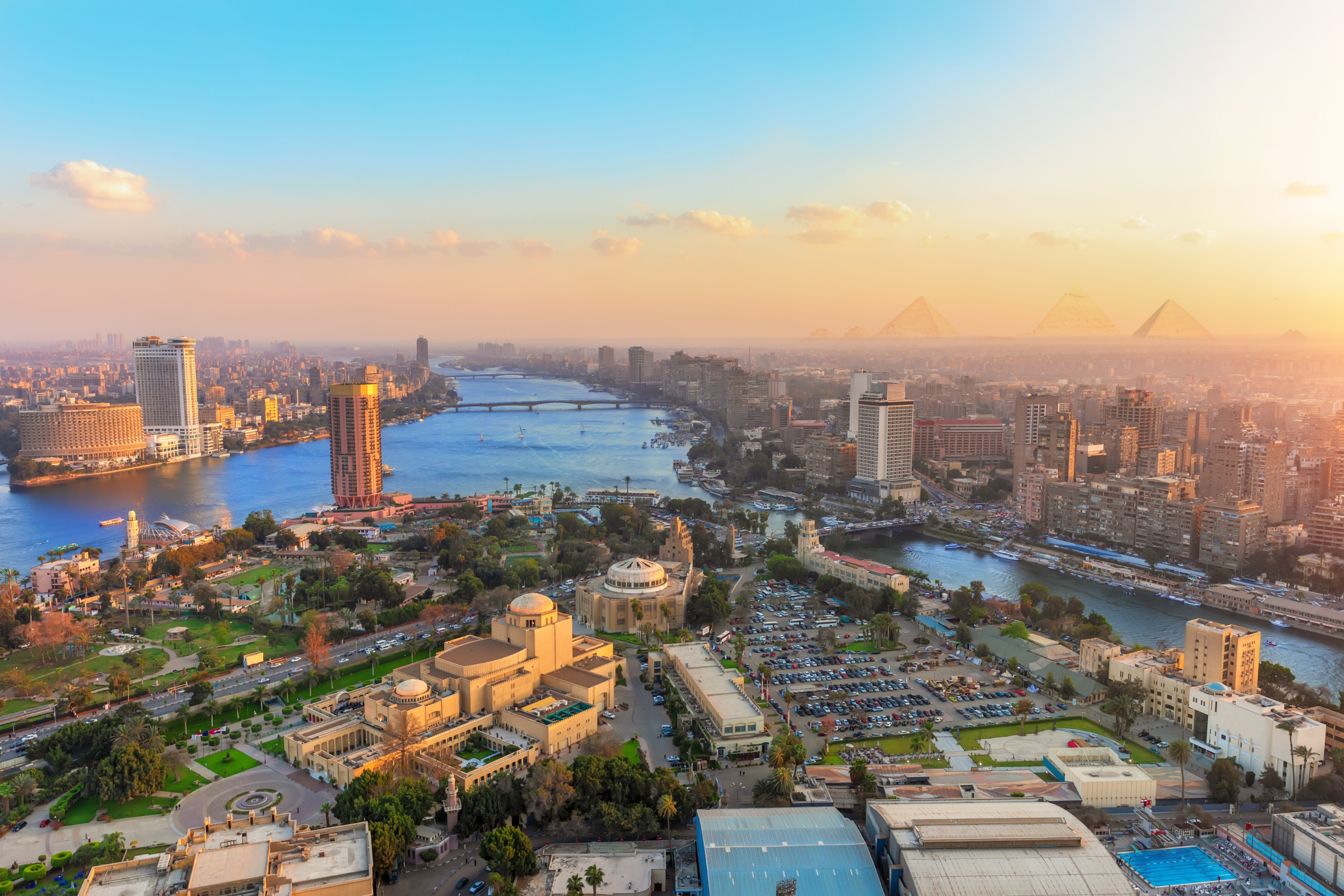 Panoramautsikt over Kairo ved solnedgang, med Nilen som renner gjennom byen og pyramidene i Giza synlige i bakgrunnen