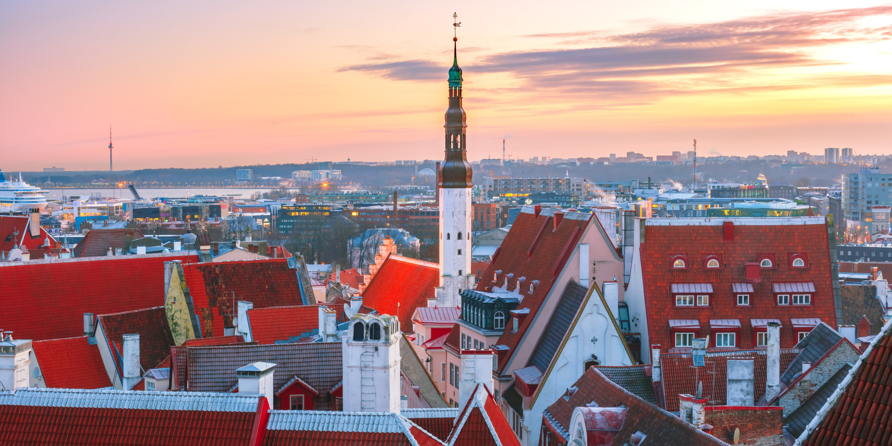 Travel to Estonia - view of Tallinn's Old Town at sunset, featuring a skyline of red-roofed medieval buildings and the prominent Town Hall spire.