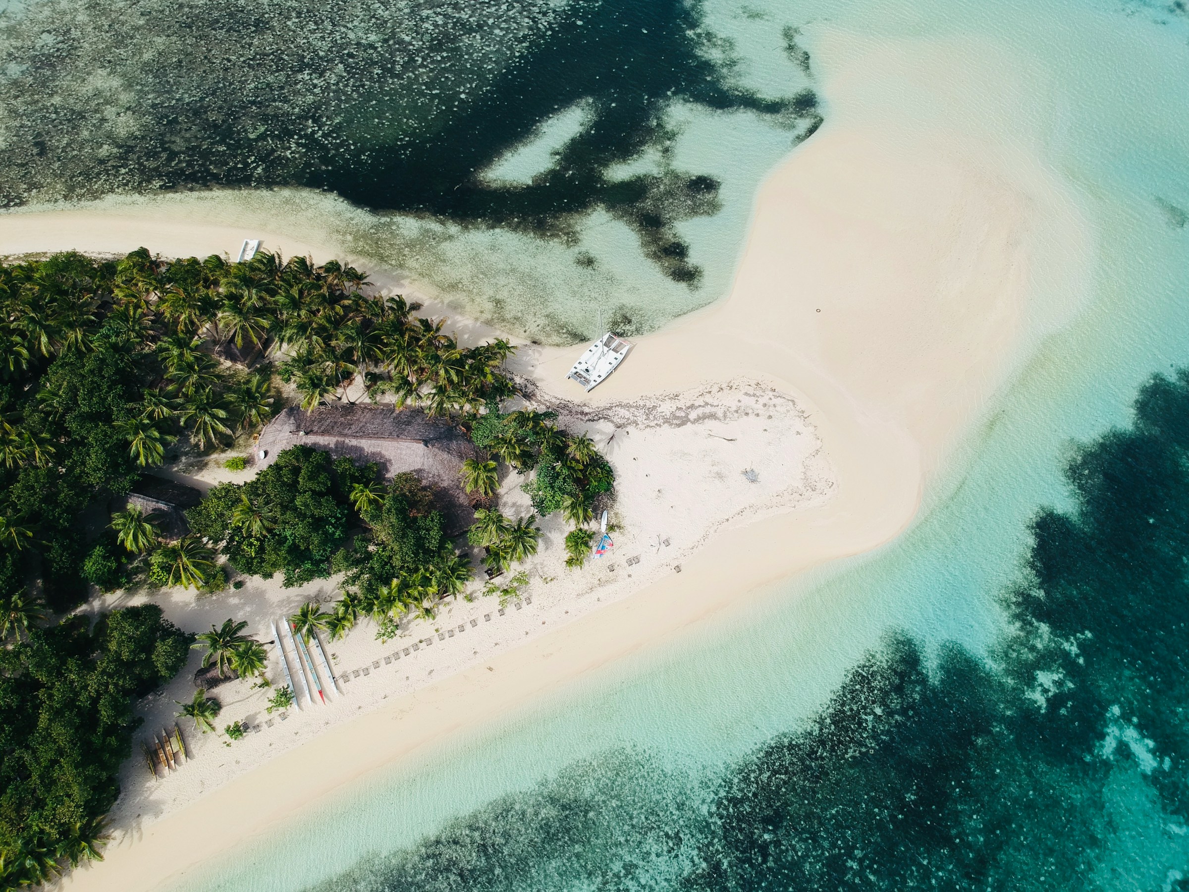 Aerial view of a tropical island with lush greenery, sandy beaches, and crystal-clear turquoise waters. A boat is anchored near the shore, surrounded by palm trees and vibrant coral reefs.
