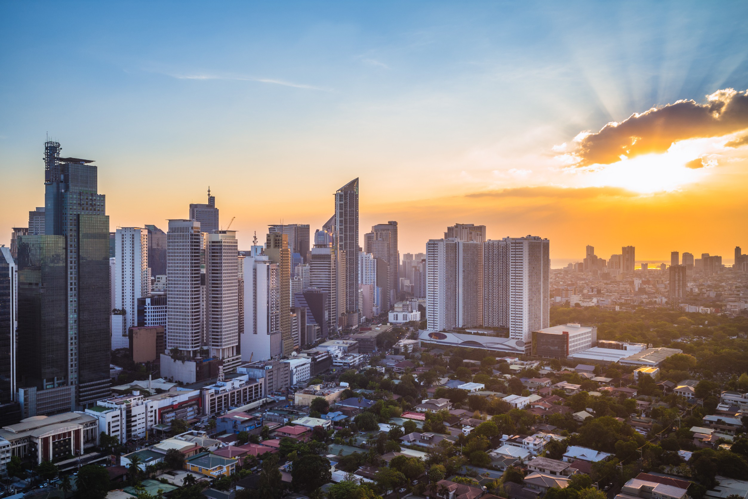 Travel to Manilla - City skyline at sunset with modern skyscrapers and a vibrant orange sky.