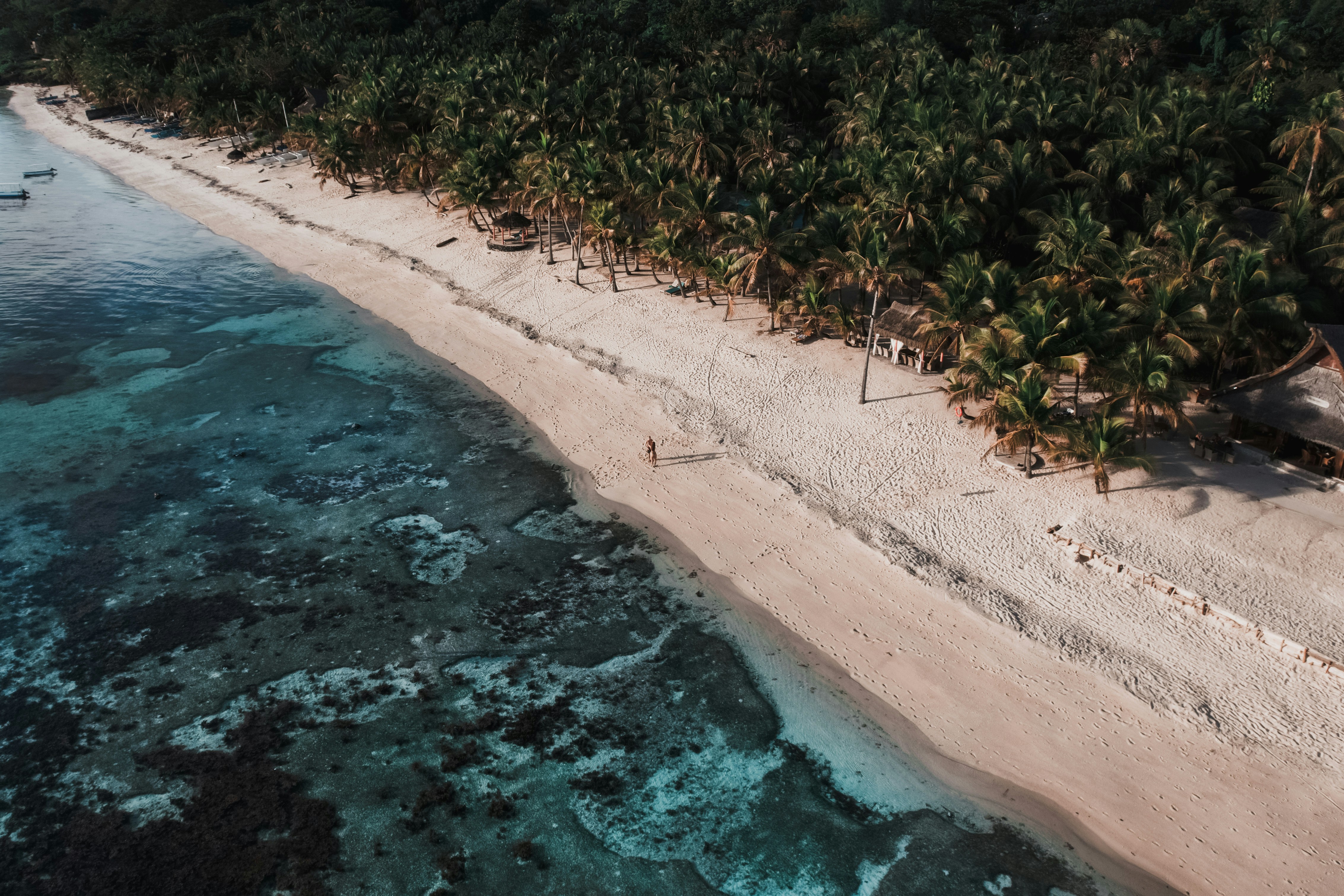 Luftfoto av en tropisk strand med hvit sand og krystallklart blått vann, omgitt av tett palmeskog