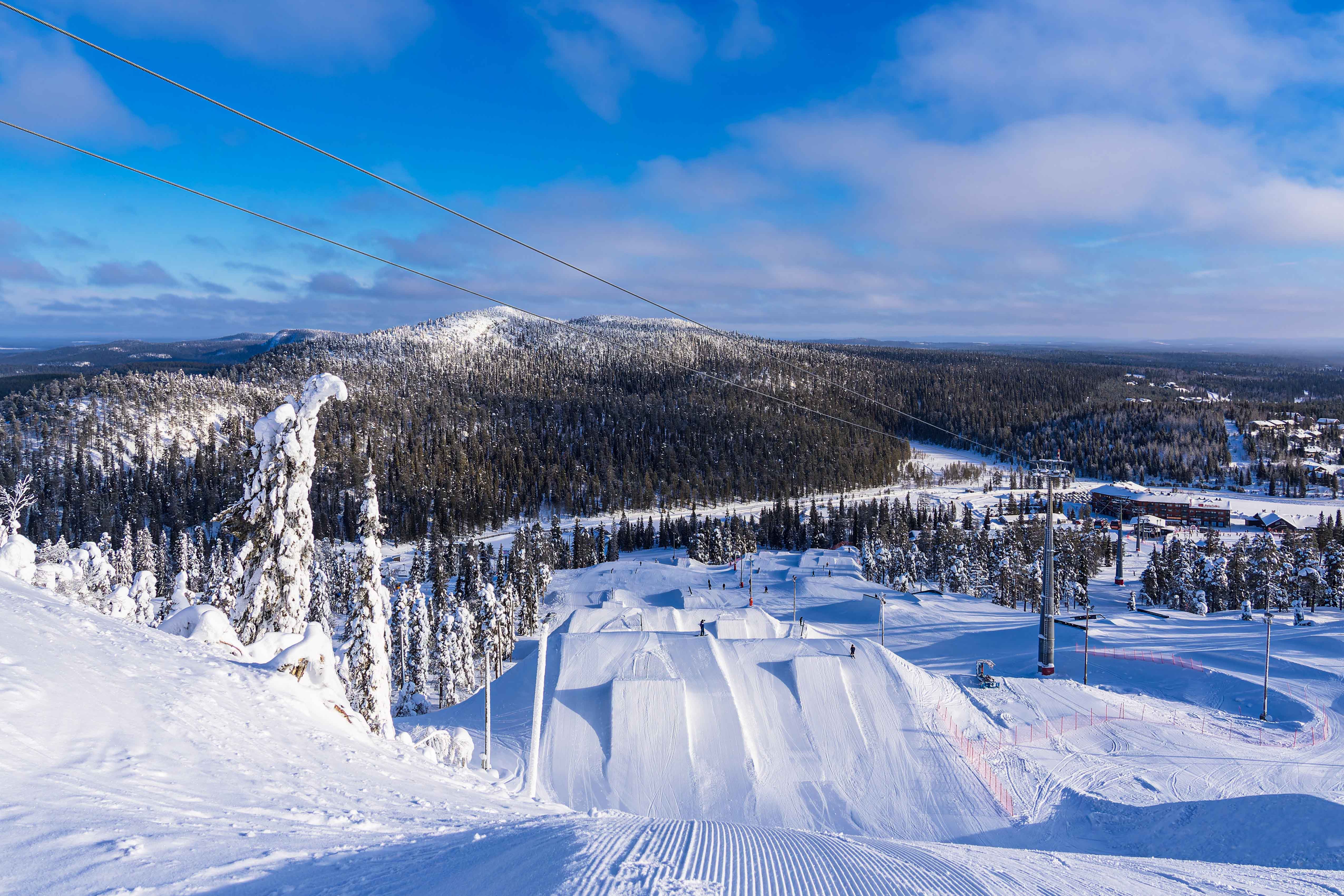 Reis til Ruka - Snødekt skiløype fører ned til tett skog og snø med blå himmel i bakgrunnen i Finland
