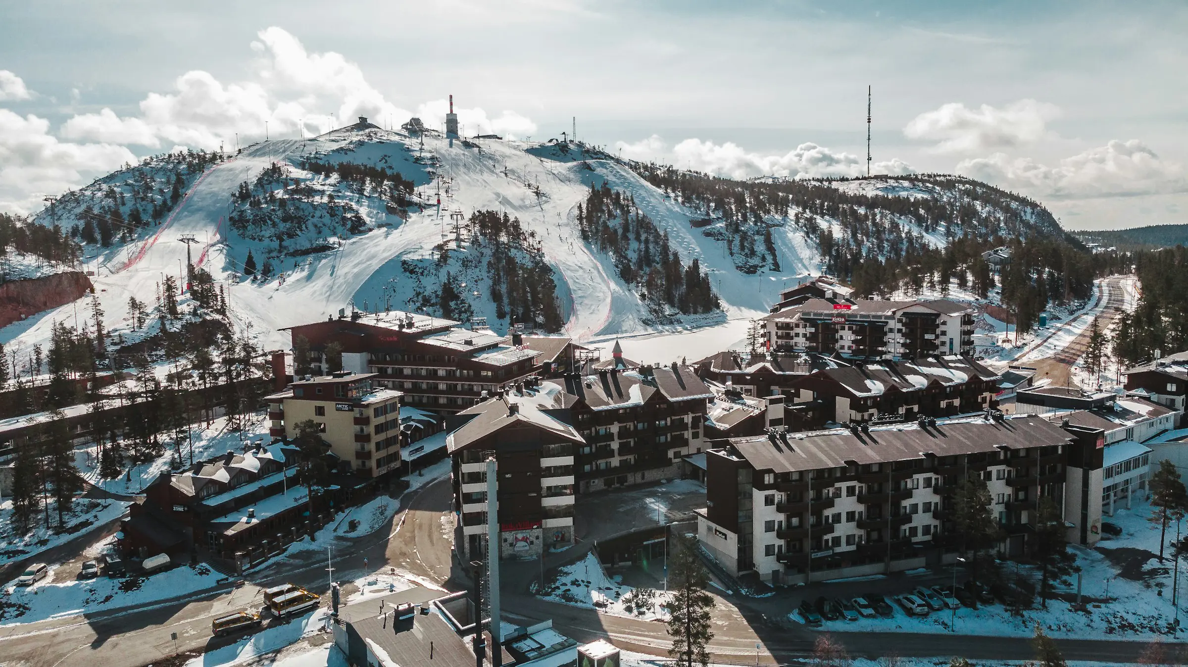 Utsikt over skibakken i Ruka, Finland som fører ned til et feriested og bygninger, alt dekket av snø