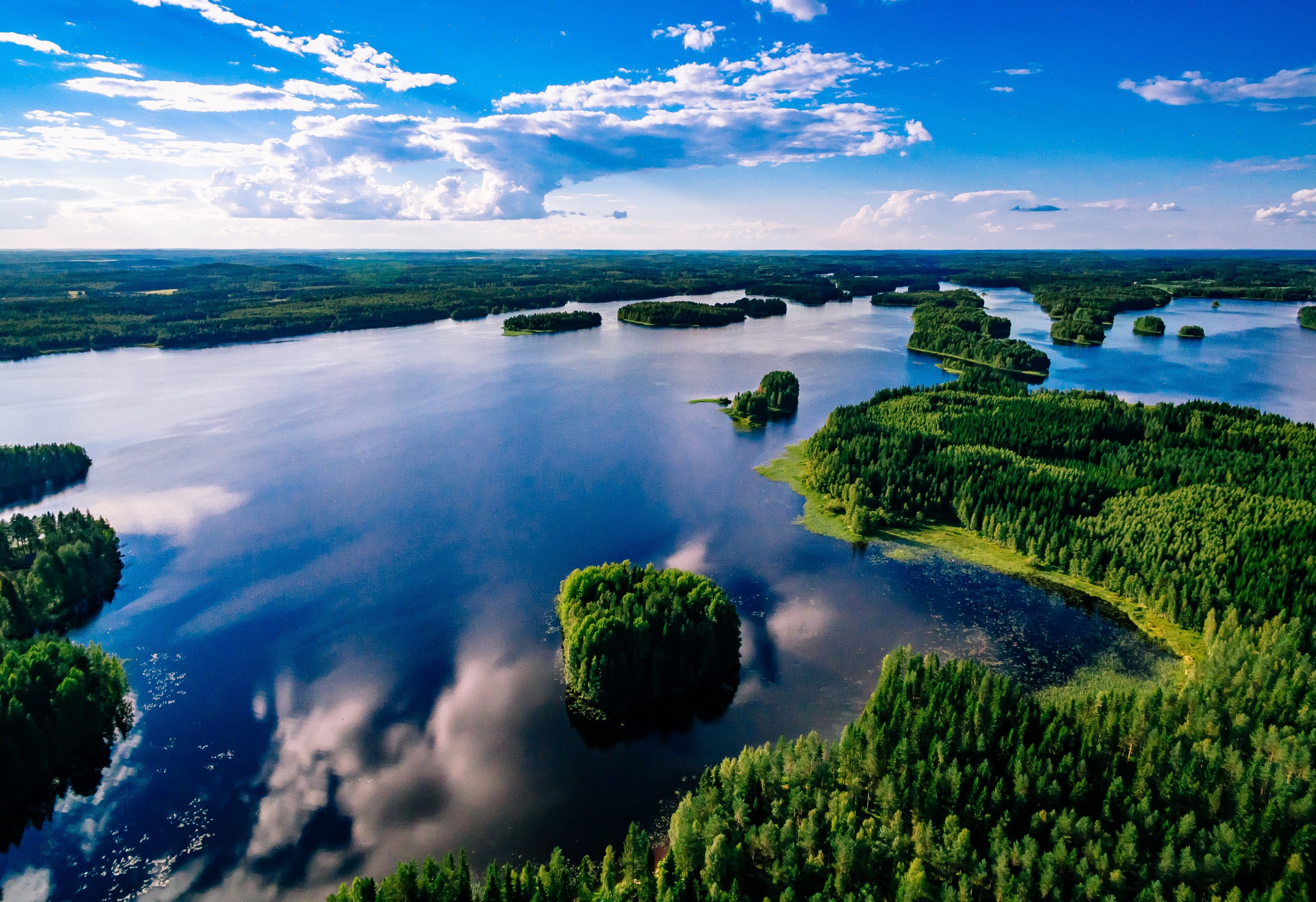 Flyfoto av en vakker innsjø med frodige grønne øyer og speilblankt vann under en klar blå himmel