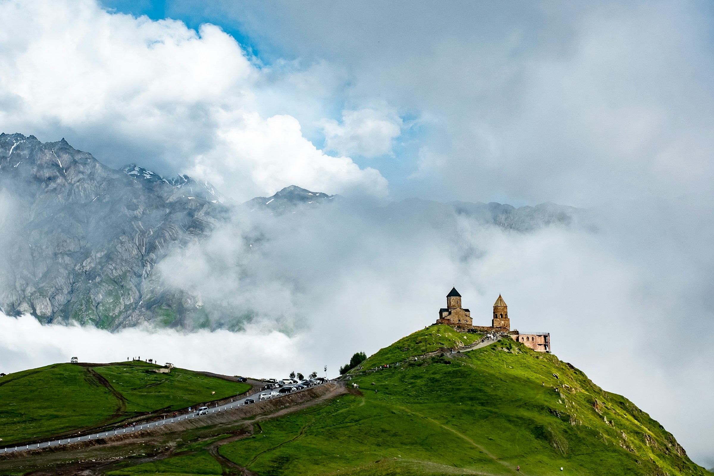 Fjelltoppkirke omgitt av frodig grønt landskap og tåkelagte fjell i bakgrunnen av Georgia.