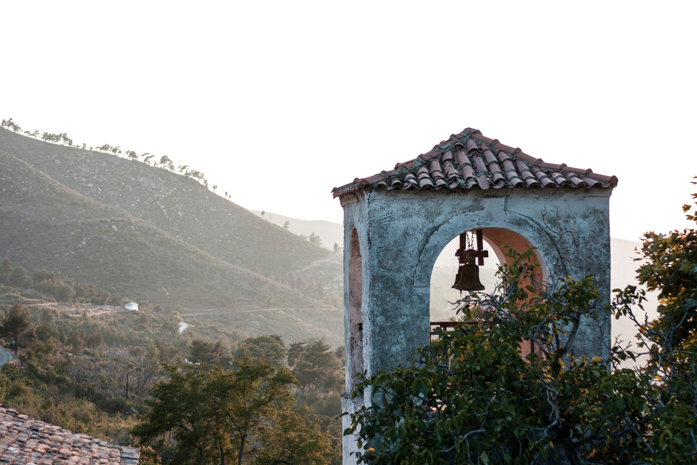 Bell tower with a tiled roof surrounded by scenic mountain landscape at sunrise.
