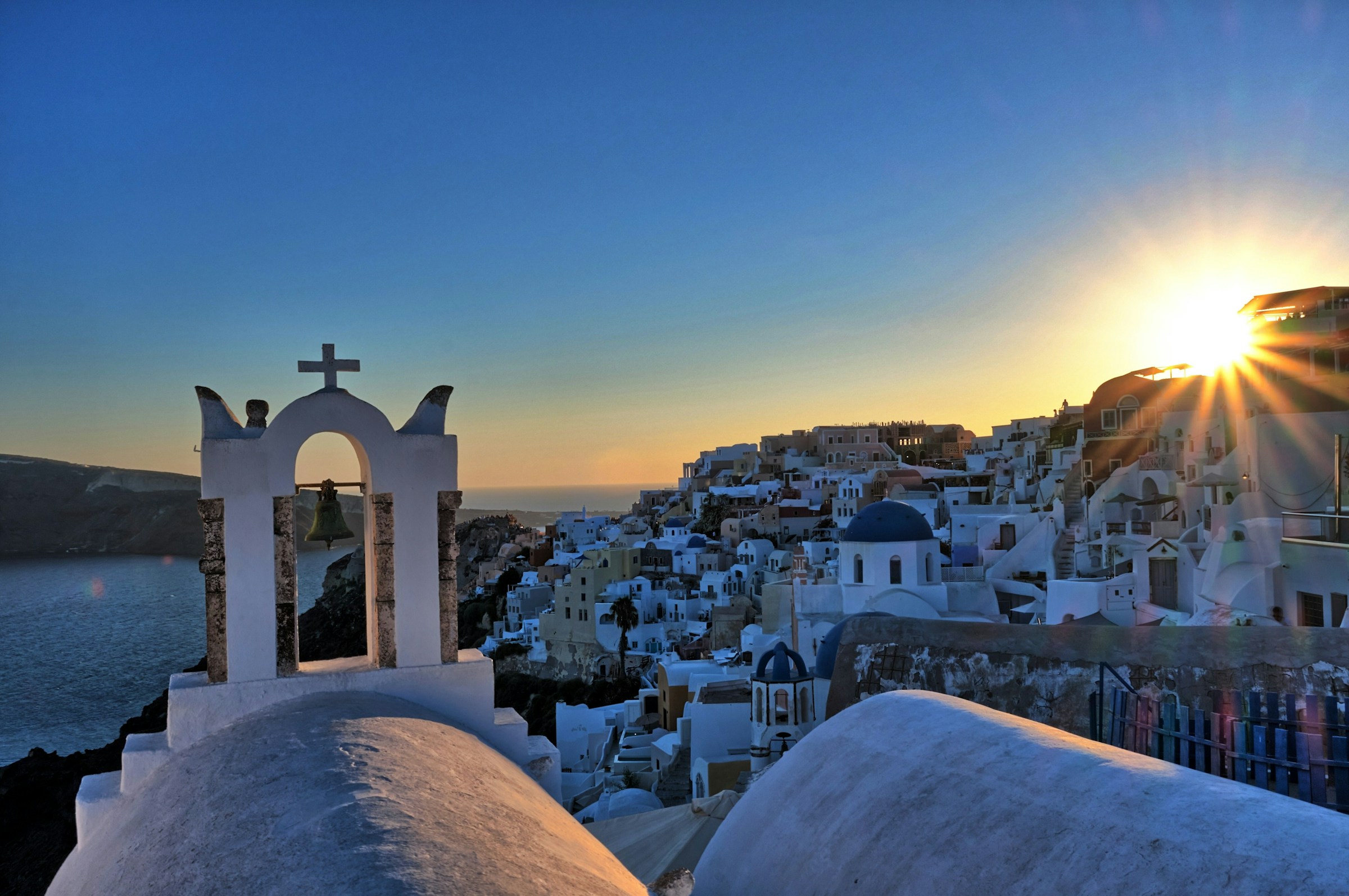 Solnedgang over Santorini, Hellas, med ikonisk hvit arkitektur og en kirke med klokketårn i forgrunnen