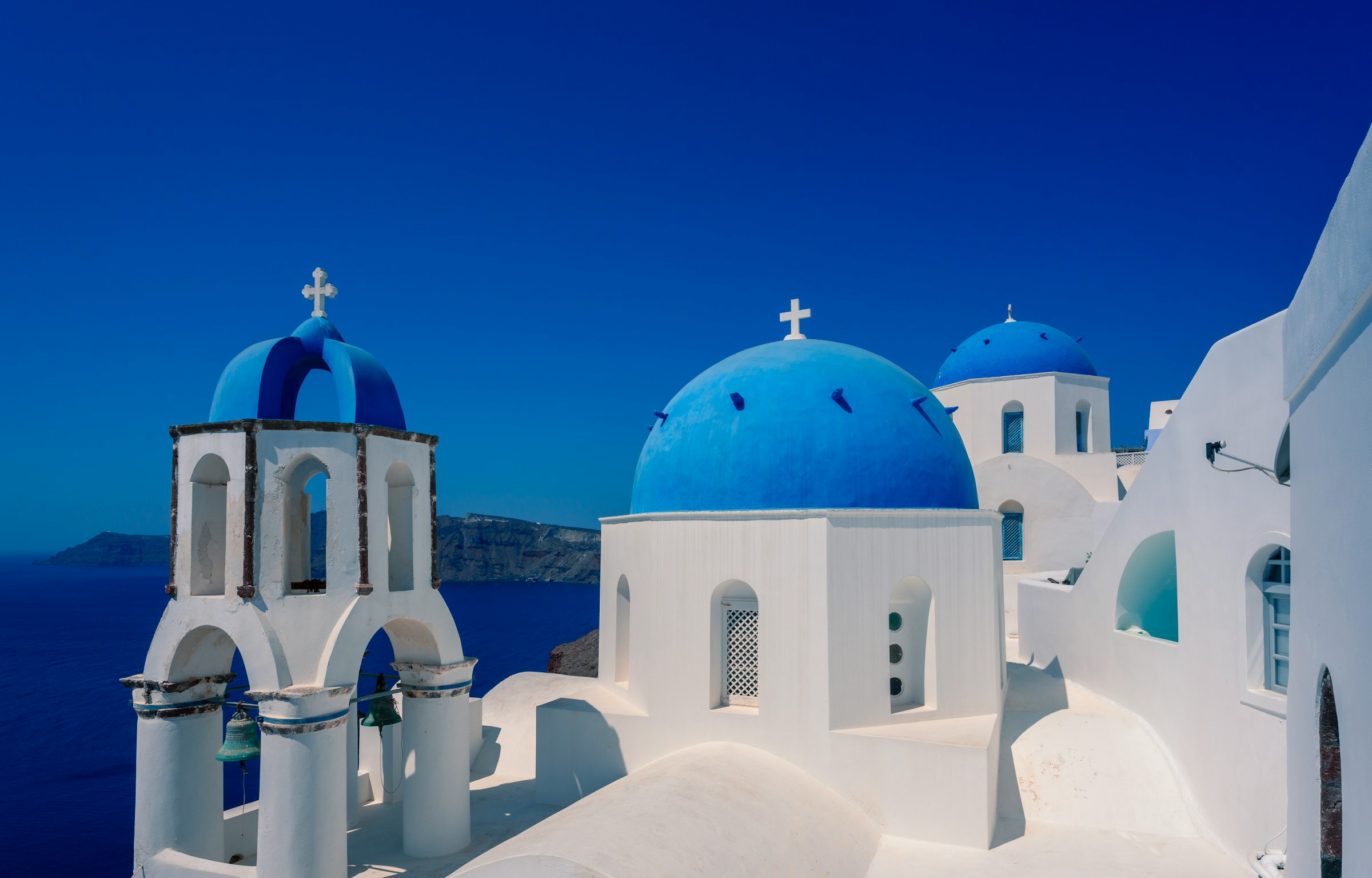 Hvite bygninger med blå kupler i Oia, Santorini, mot en klar blå himmel og Egeerhavet i bakgrunnen