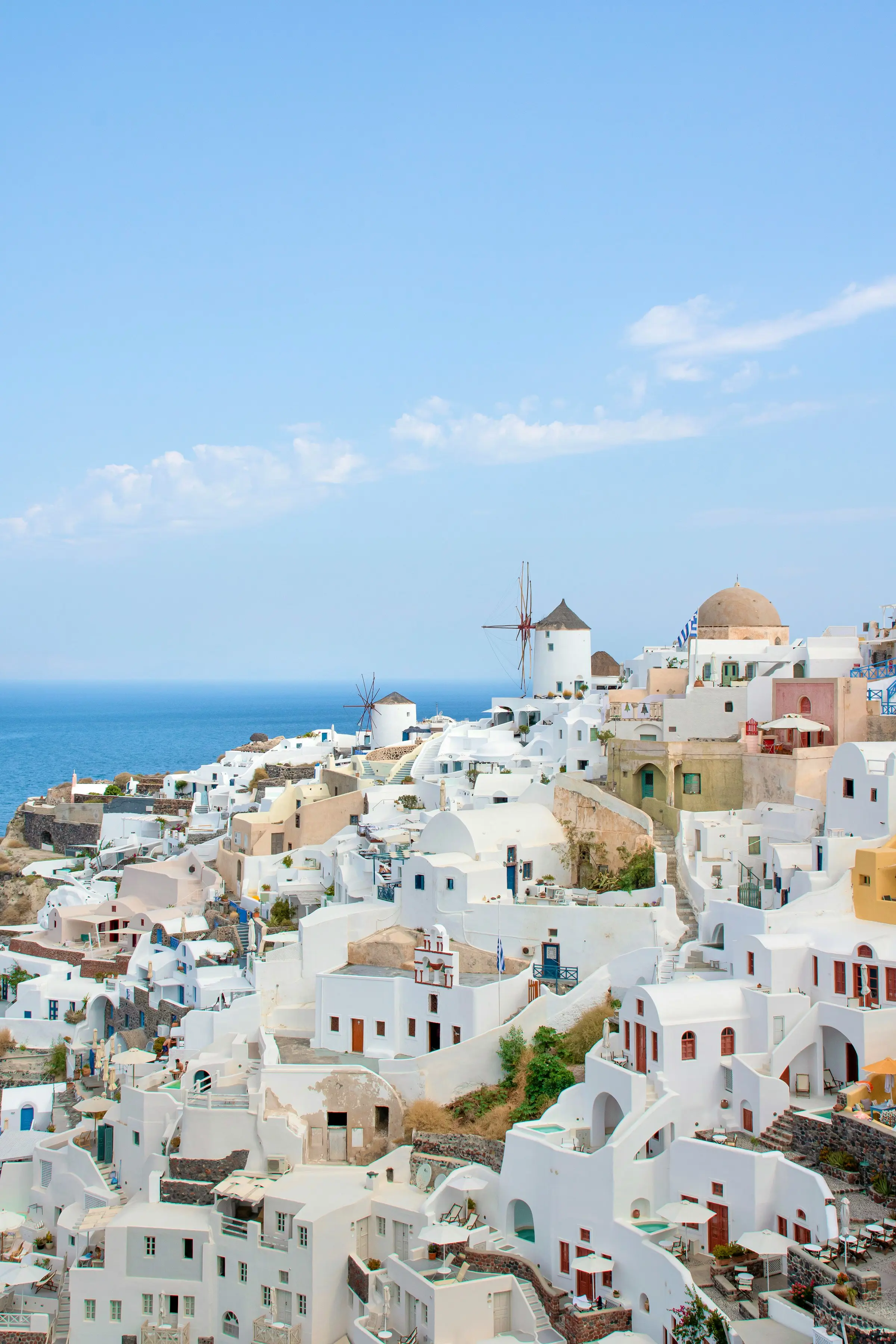Hvite bygninger i Oia, Santorini, med tradisjonelle vindmøller og en blå himmel i bakgrunnen