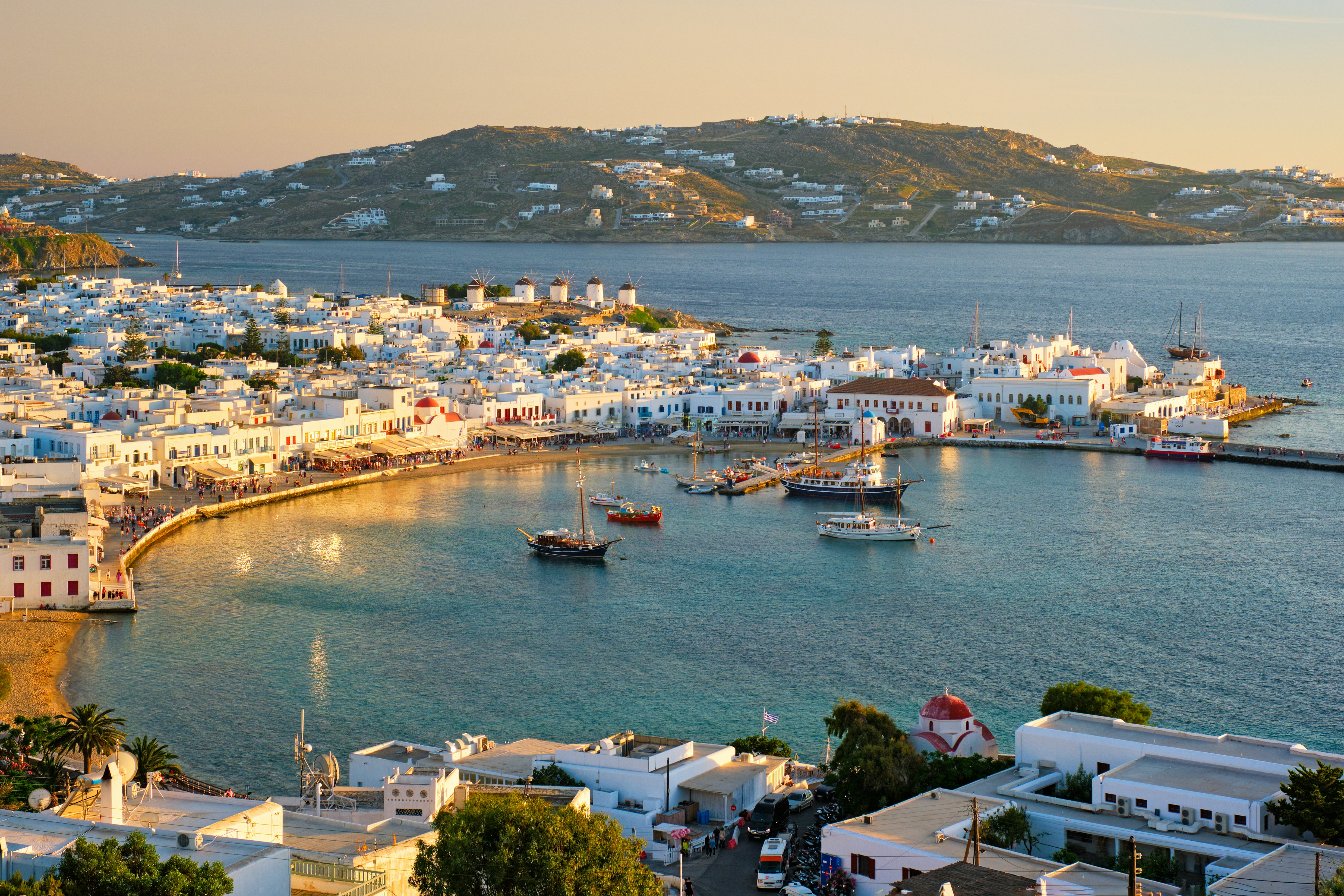 Kystlinje av Mykonos by i solnedgang, med hvitkalkede bygninger og tradisjonelle vindmøller ved havnen, Egeerhavet i bakgrunnen