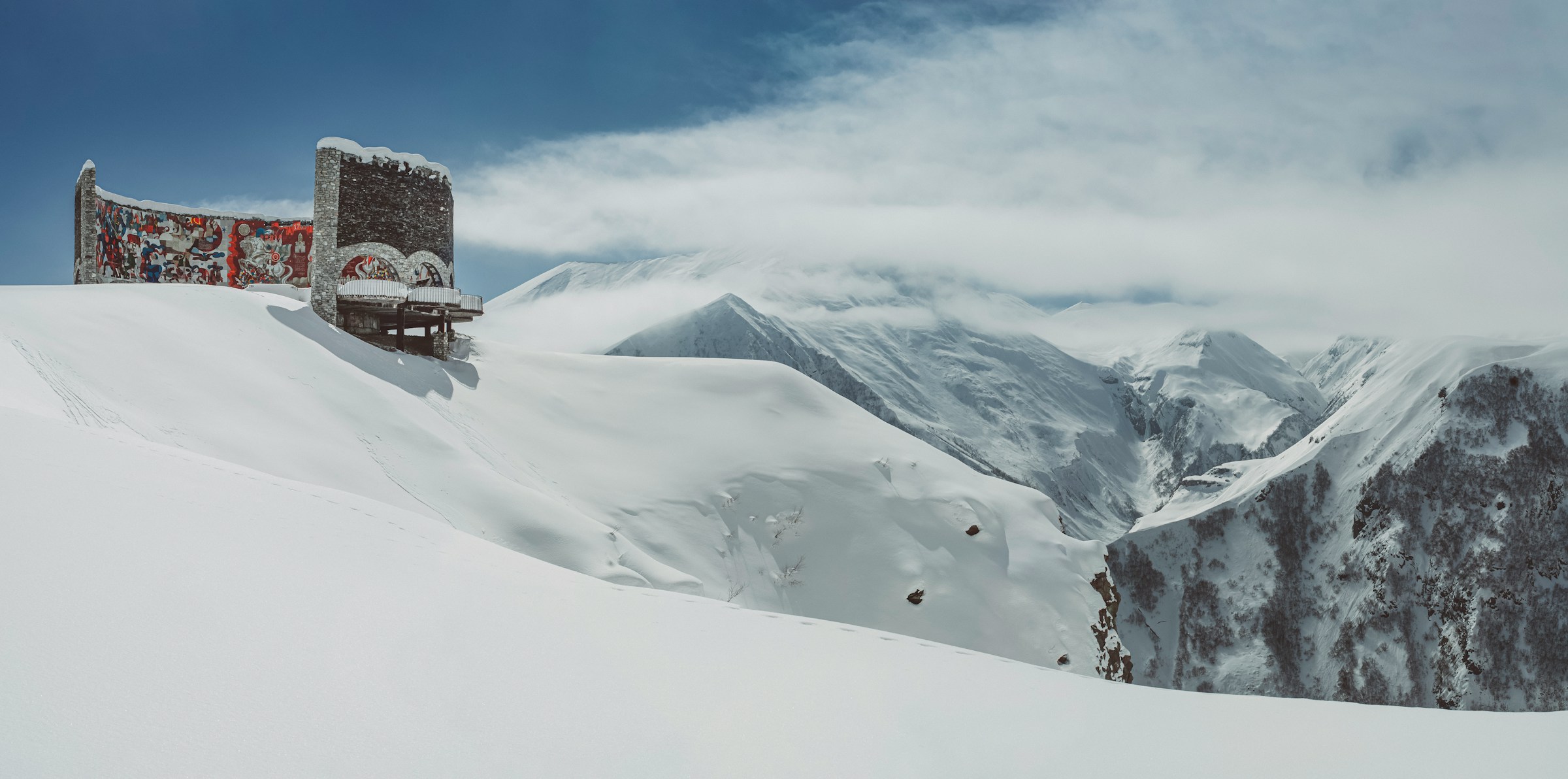 Snødekt fjellandskap med fargerik utsmykket bygning og overskyet himmel i bakgrunnen, vakkert og fjernt vinterlandskap.
