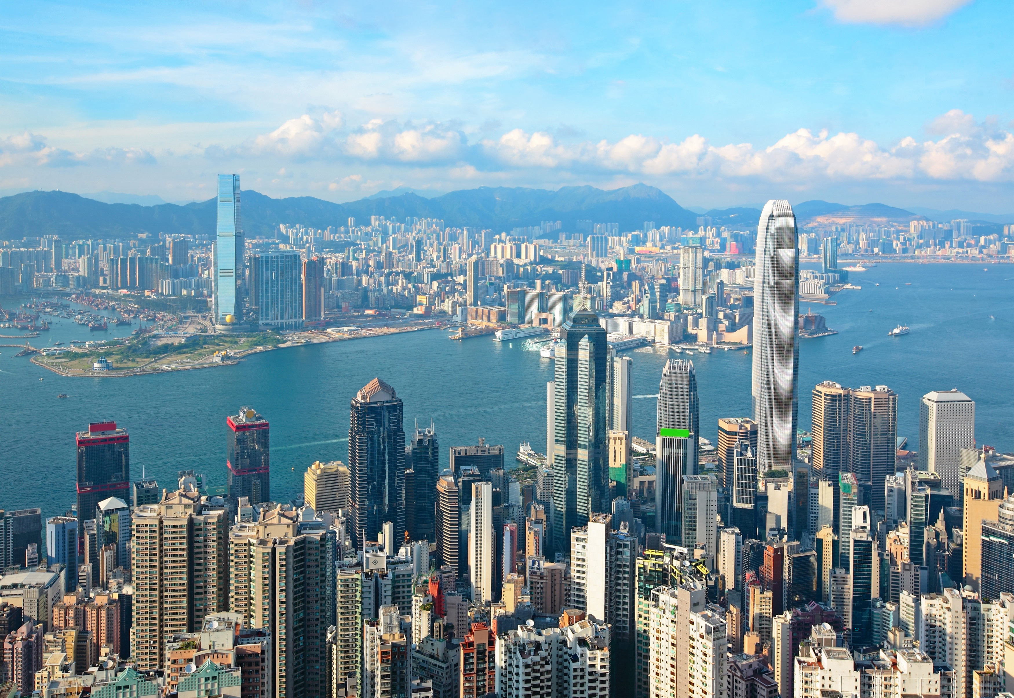 Travel to Hong Kong - Aerial view of Hong Kong skyline showcasing skyscrapers, Victoria Harbor, and distant mountains.