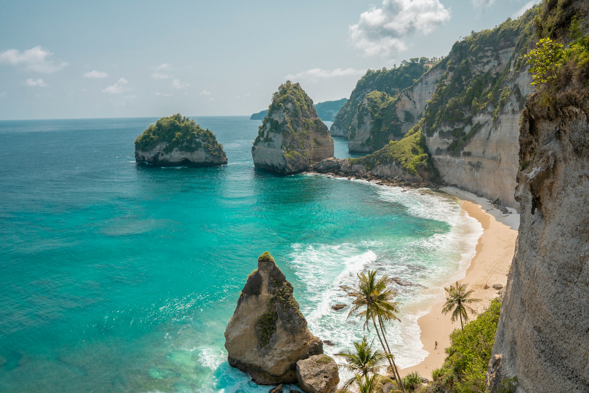 Scenic view of a tropical beach with turquoise water and dramatic rock formations surrounded by lush greenery on a sunny day.