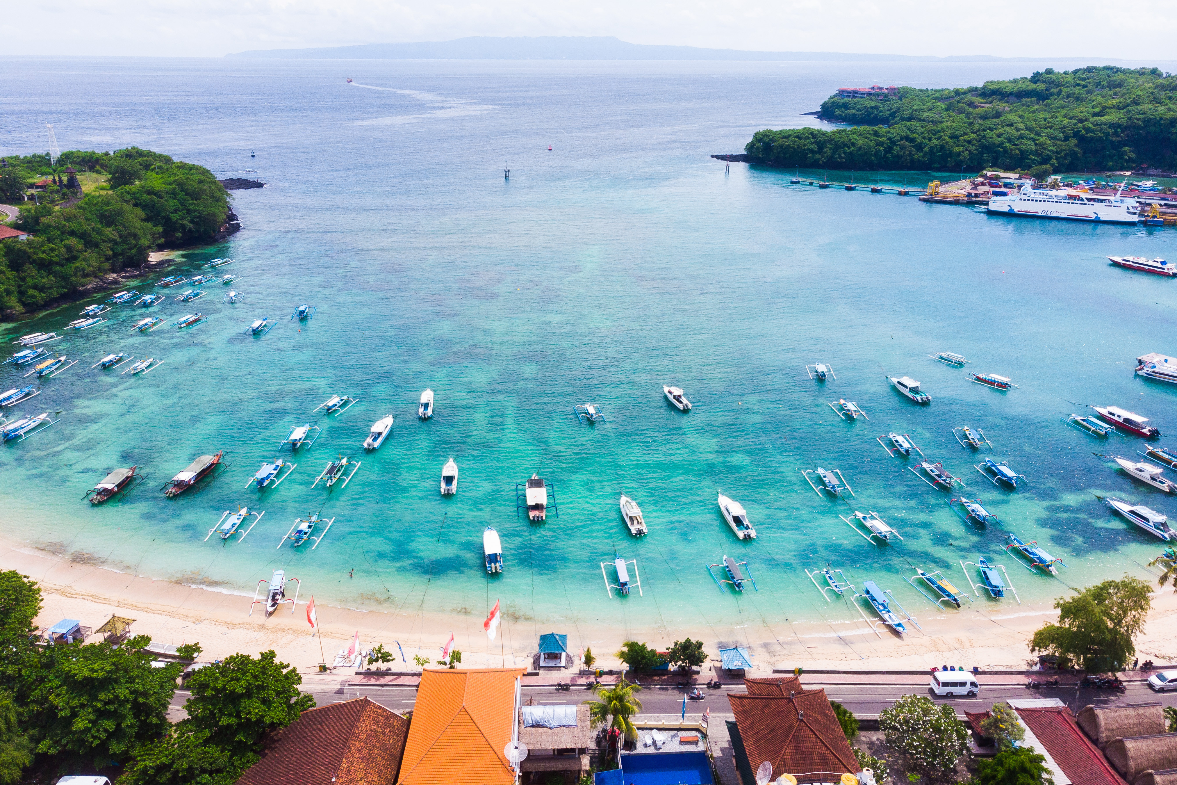 Travel to Bali - Aerial view of a tropical beach with clear turquoise waters and numerous boats anchored near the shore.