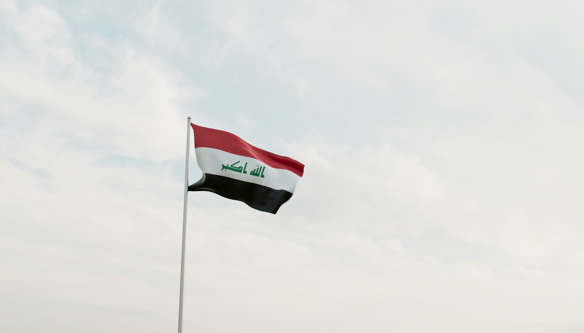 Iraqi flag waving in the sky against a backdrop of clouds.