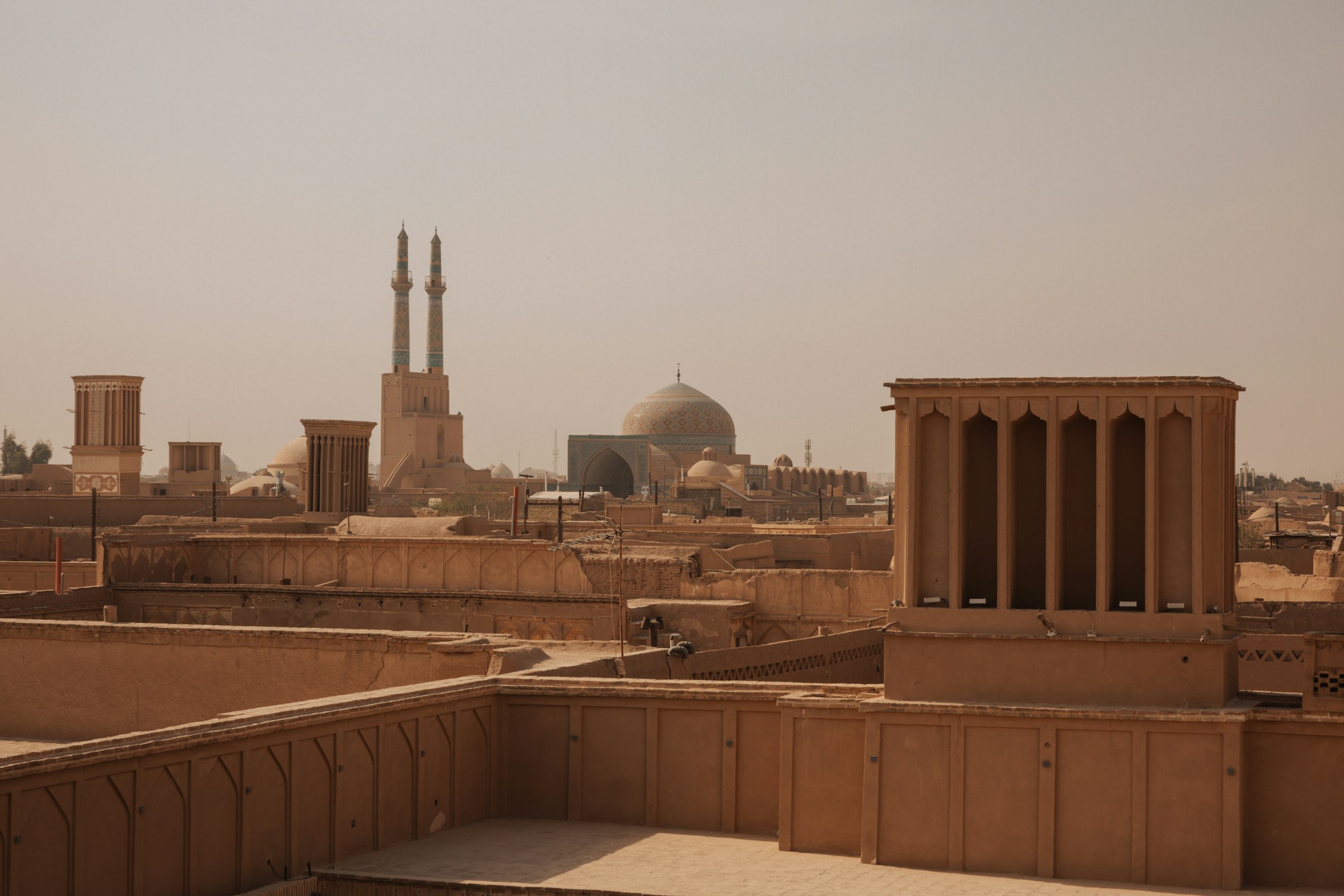 Historic skyline of Yazd, Iran, featuring traditional windcatchers and the iconic Jameh Mosque domes under a clear sky.